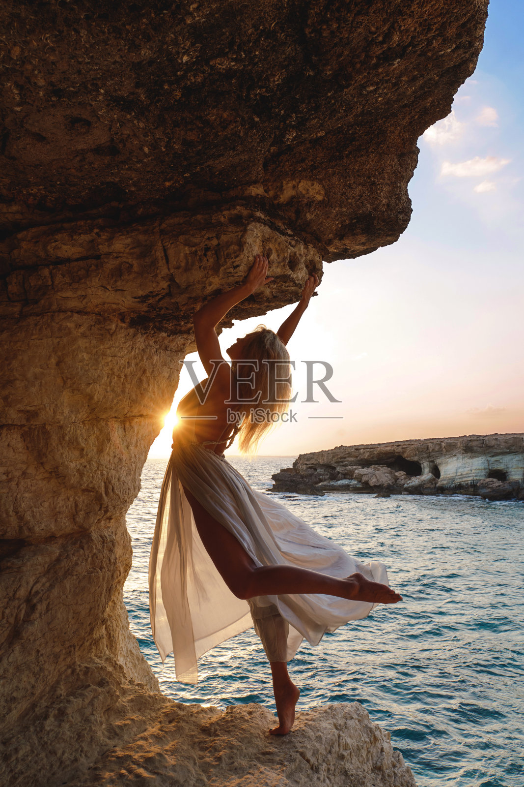 日落时分，悬崖上身穿飘逸丝绸长裙的女子照片摄影图片