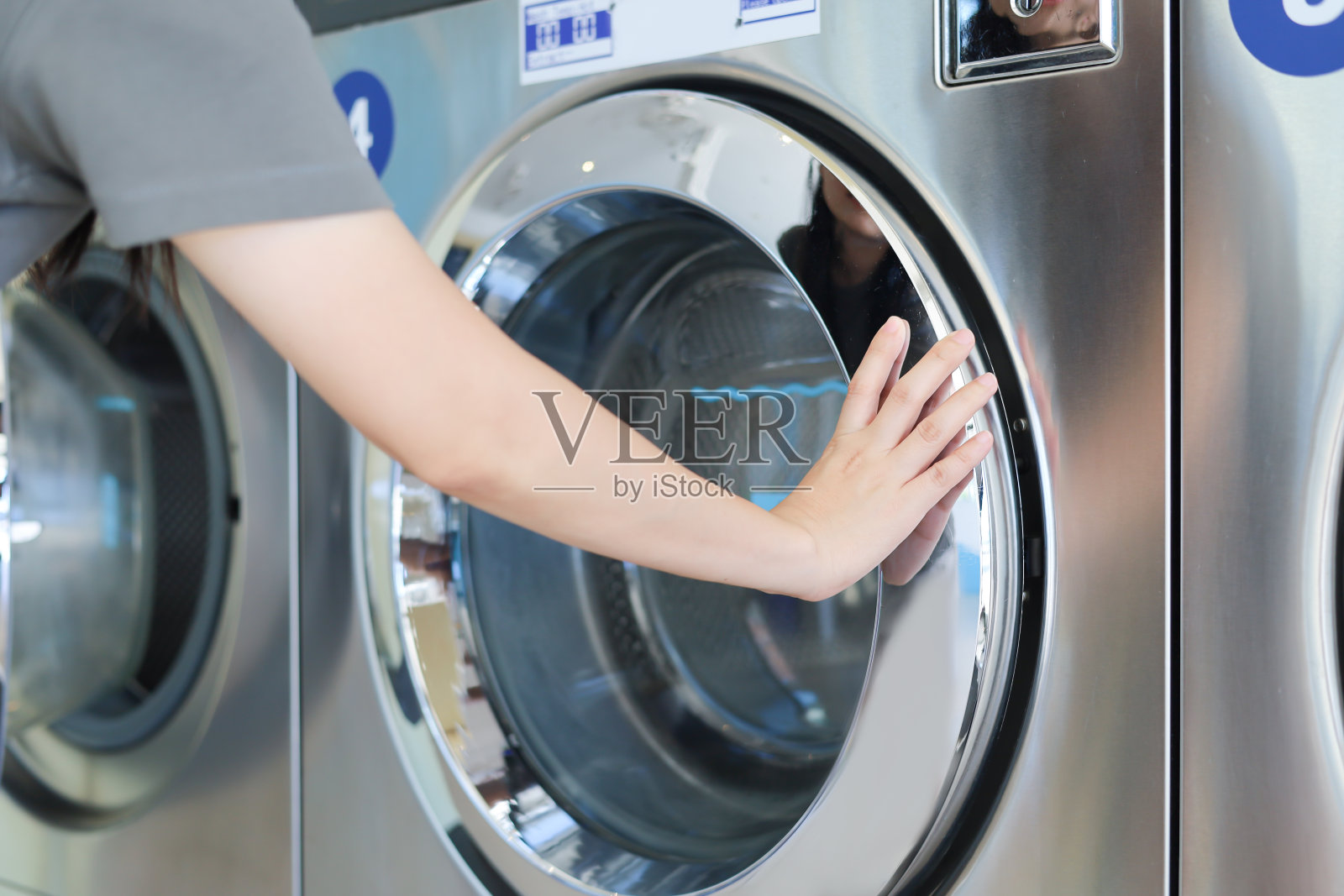 年轻的妇女正在合上洗衣机盖洗衣服。公共自助洗衣店的工业洗衣机。自助洗衣设施，配备多台自动洗衣机。照片摄影图片