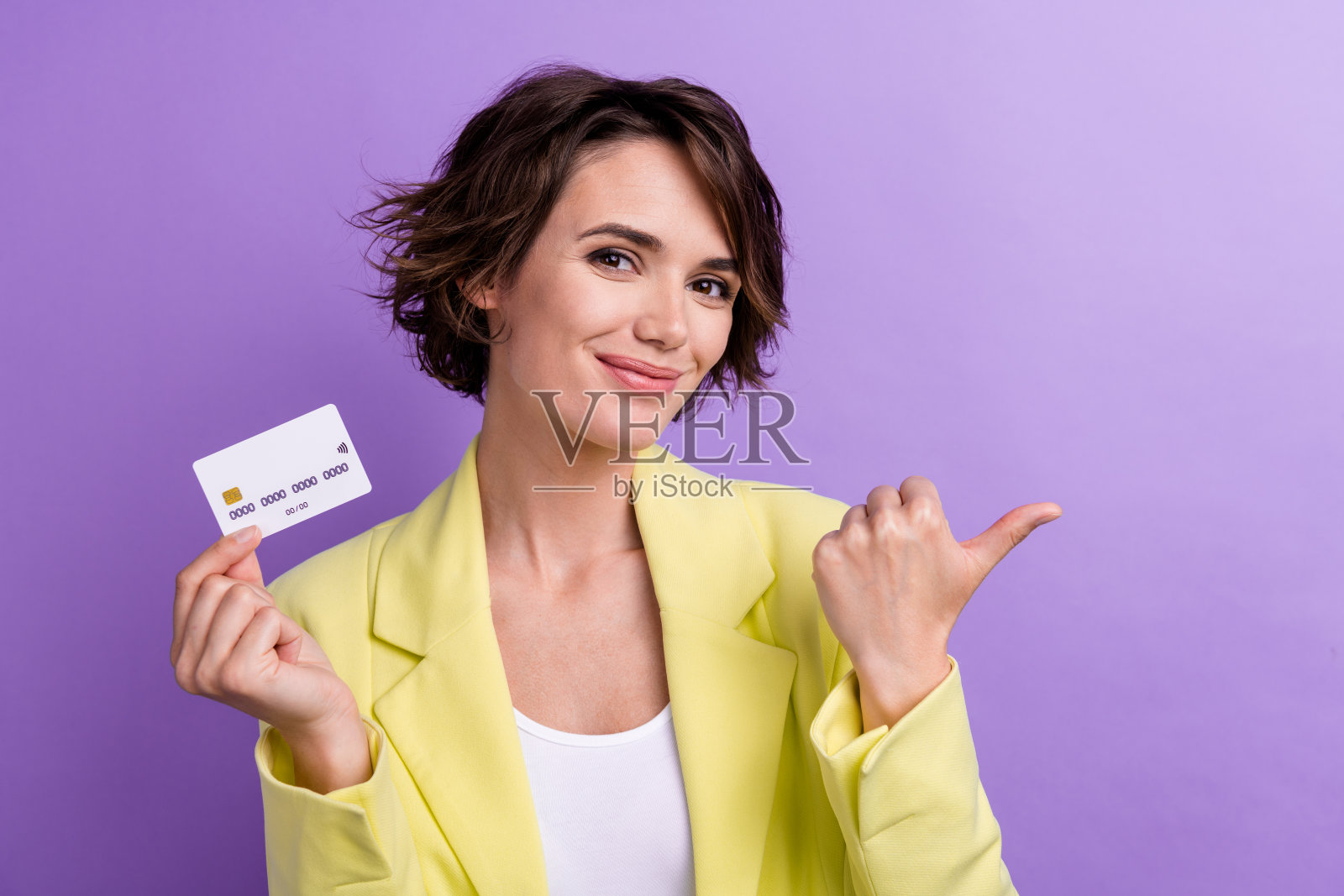 年轻女孩穿着黄色西装的照片，手指指向样板，富有的投资者推荐的新项目孤立在紫色背景上照片摄影图片