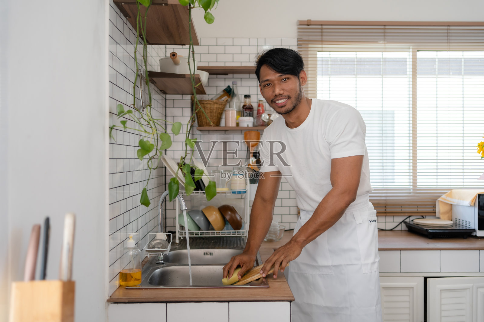 一名亚洲男子在家里做完饭后，正兴高采烈地准备把厨具清洗干净。照片摄影图片