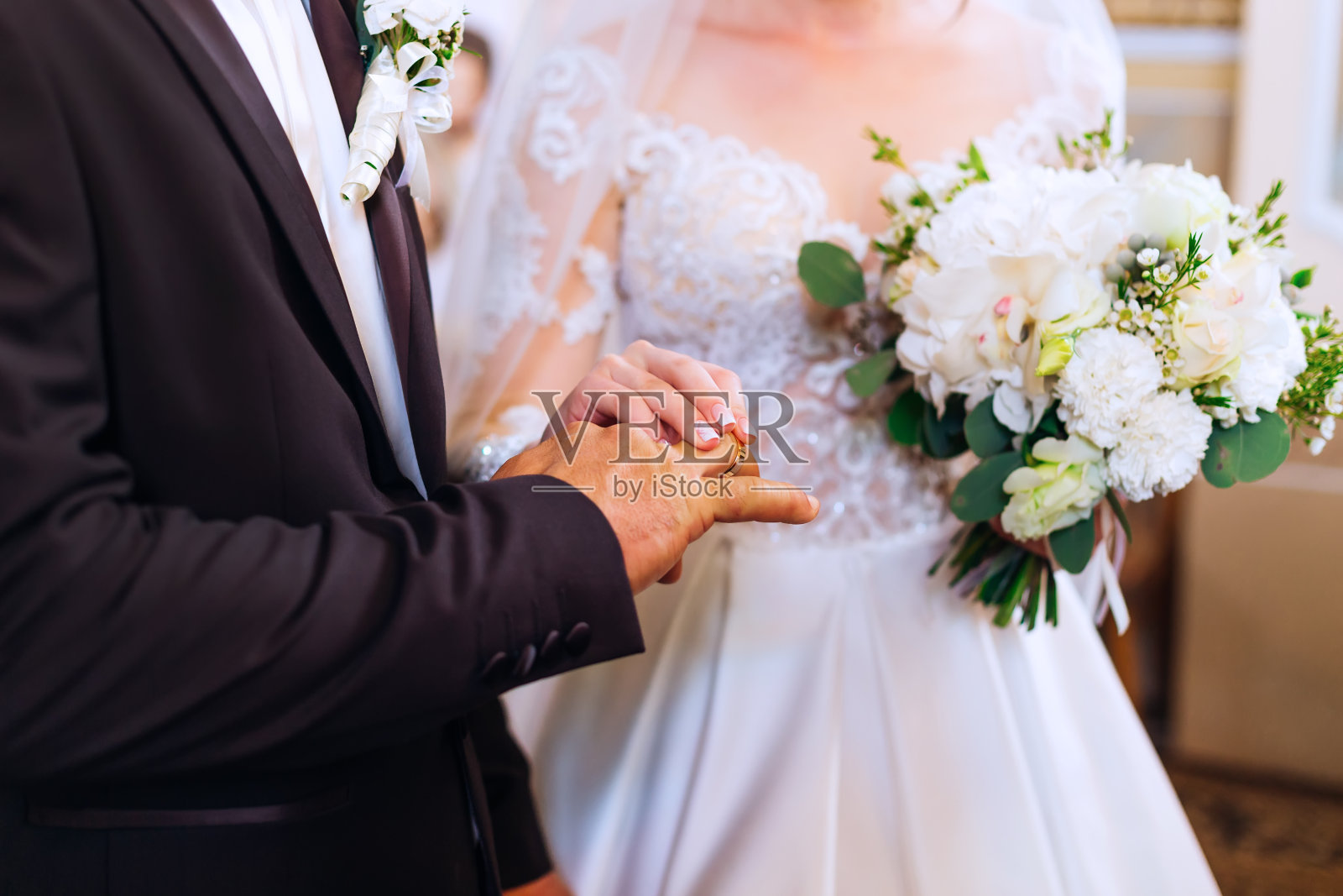 身穿白色婚纱的新娘手持别致的婚礼花束，新郎站在她旁边，交换结婚戒指照片摄影图片