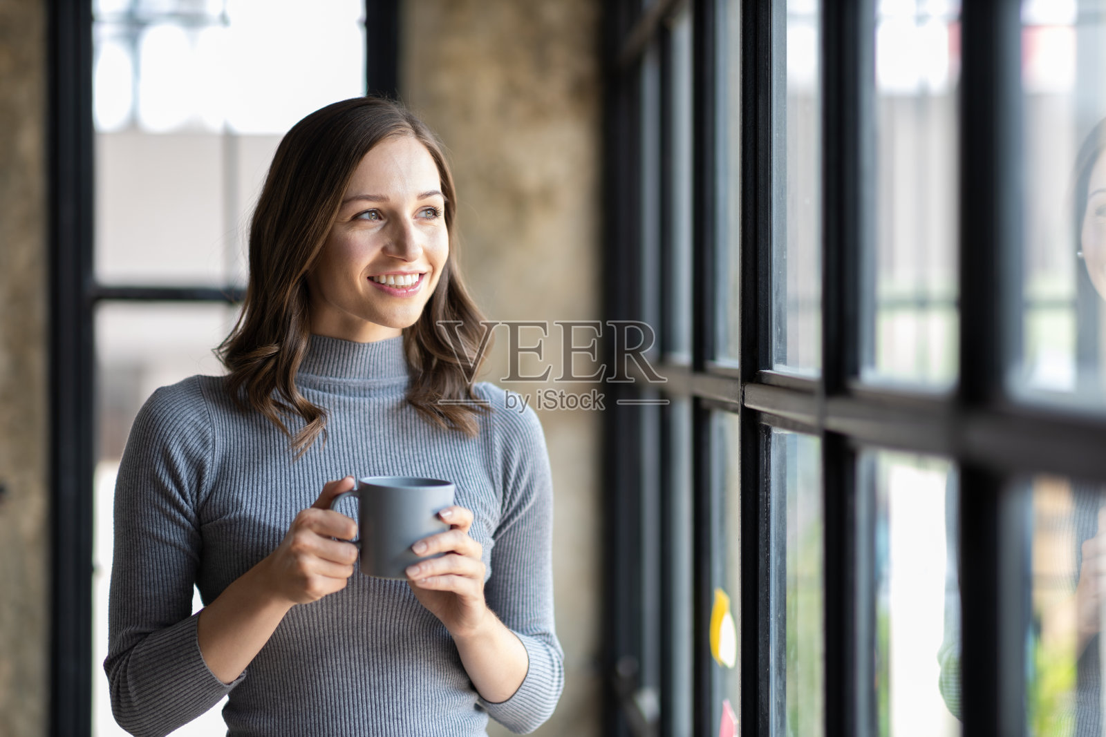 一个迷人的女人在房子的窗户边喝着早晨的咖啡。照片摄影图片