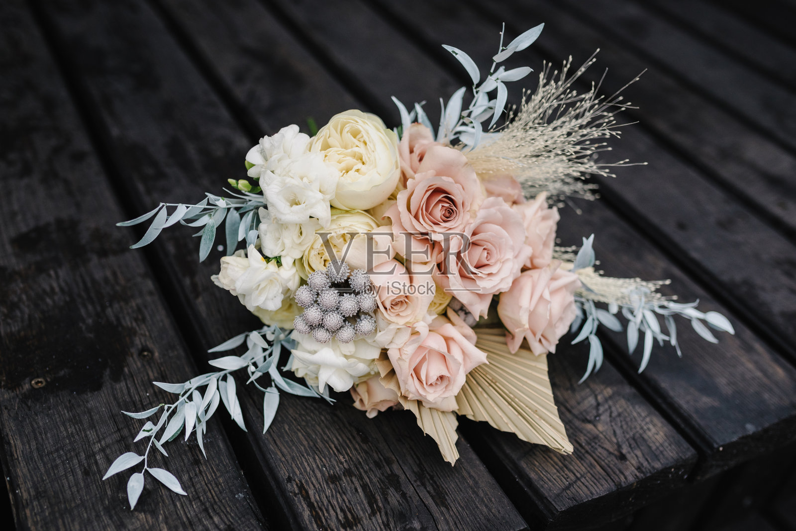 花束用白色和粉红色的花，玫瑰，绿色，装饰羽毛和装饰植物，叶子。木制背景上装饰着鲜花和绿色丝带的婚礼花束。前视图。特写镜头。照片摄影图片