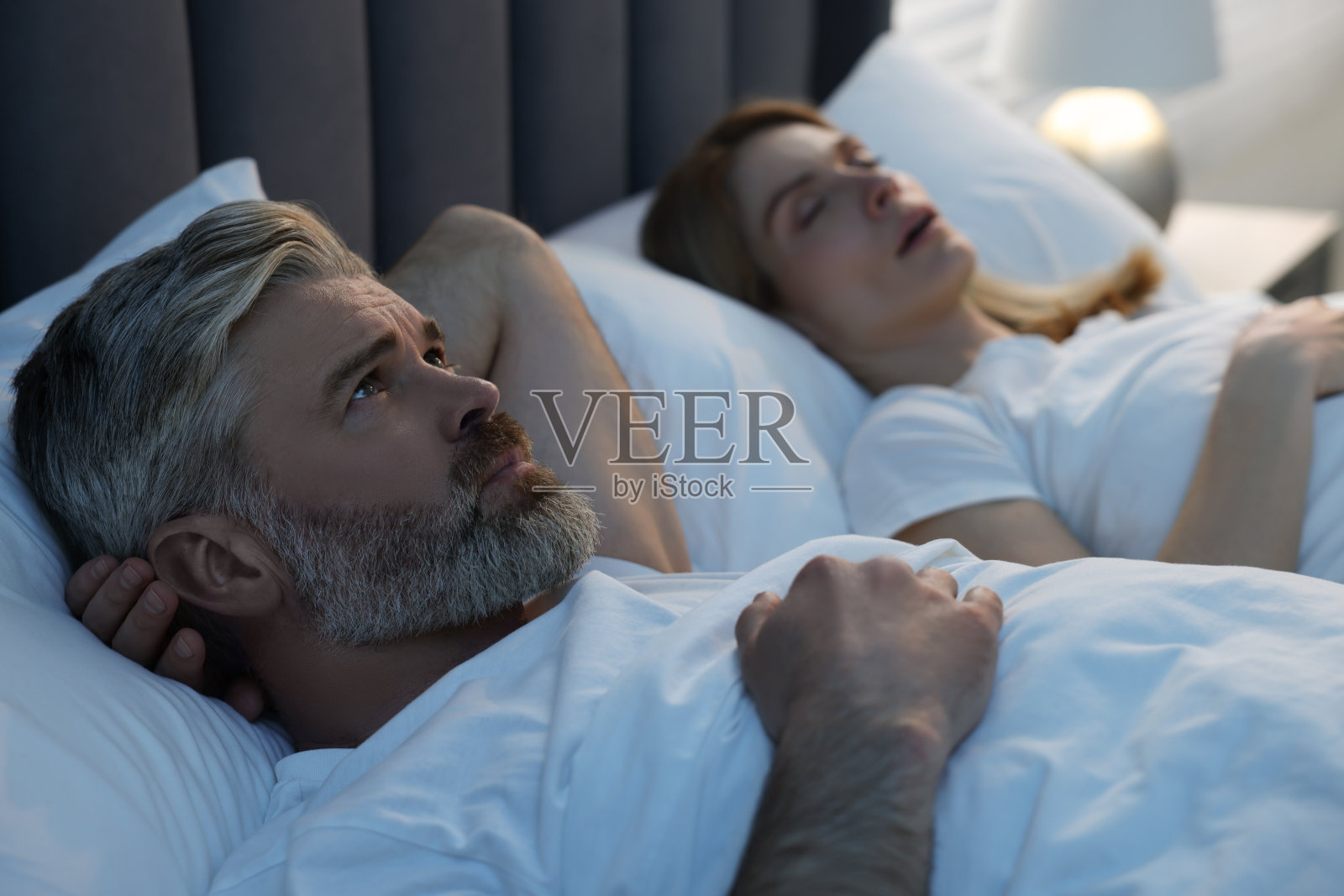 恼怒的男人躺在家里打鼾的妻子旁边照片摄影图片