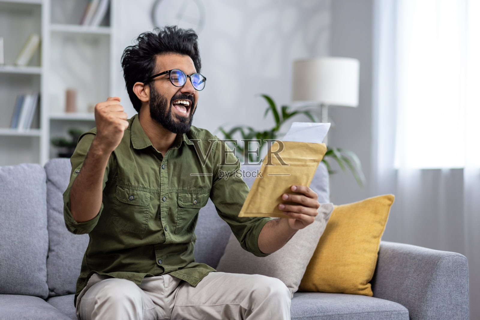 喜洋洋的西班牙人收到了信件邮件通知，男子坐在家里客厅的沙发上拿着信封微笑着阅读照片摄影图片