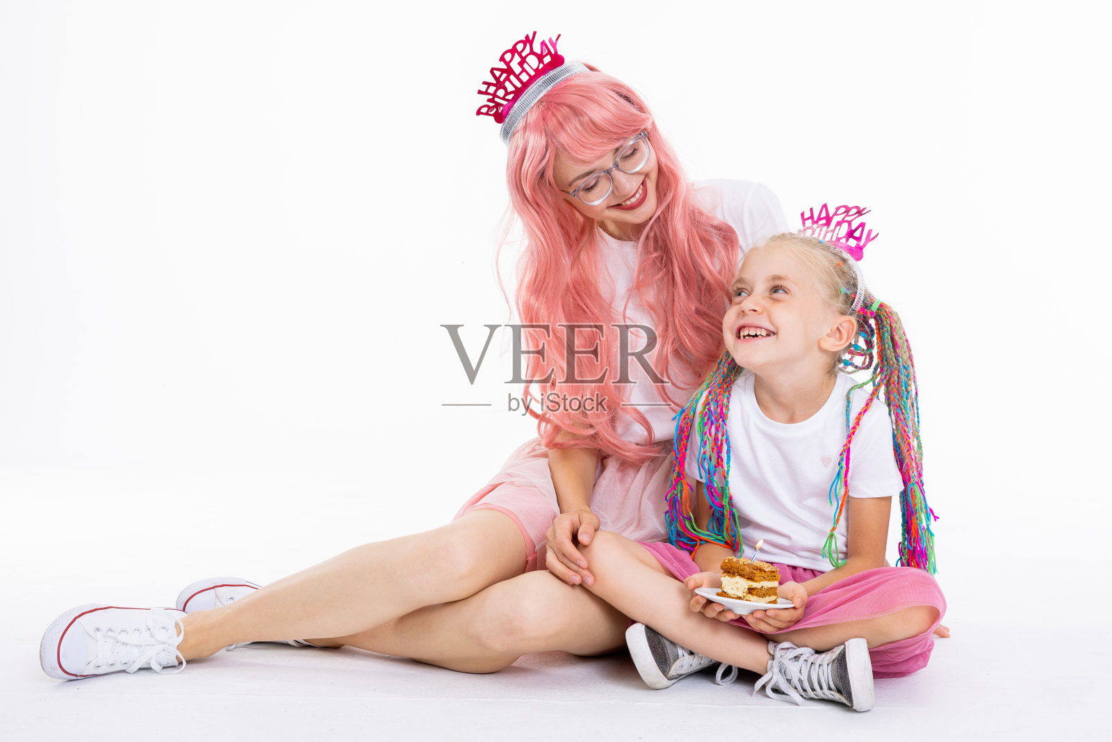 快乐的学龄前女儿孩子坐在莲花的姿势，年轻的现代母亲手里拿着蛋糕和蜡烛，穿着时髦的衣服和有趣的发型照片摄影图片