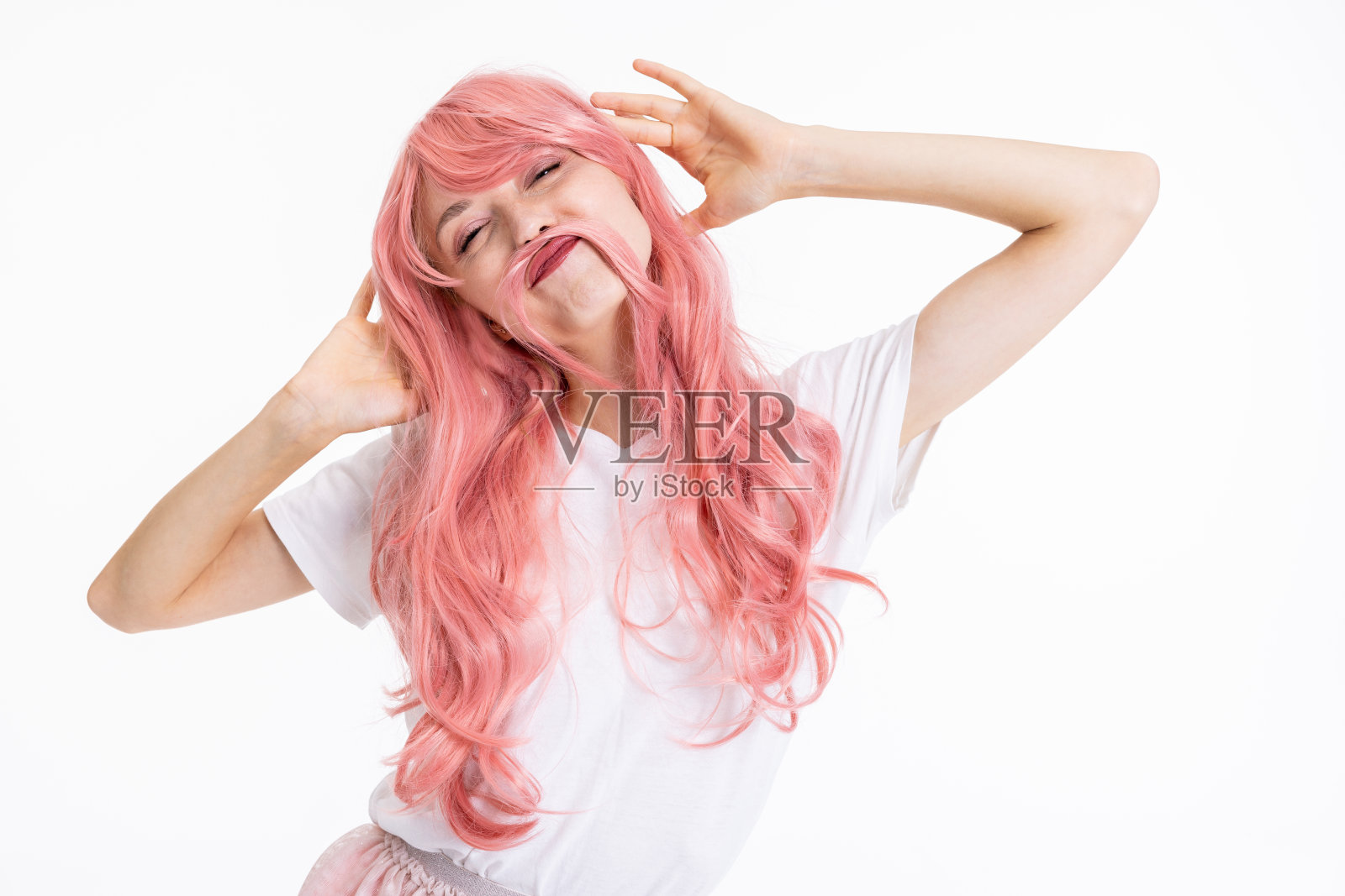开朗美丽的年轻母亲女孩的肖像，戴着粉红色的假发，在白色的背景上滑稽地摆姿势，为时尚杂志拍照，穿着普通的白色t恤和粉红色的裙子照片摄影图片