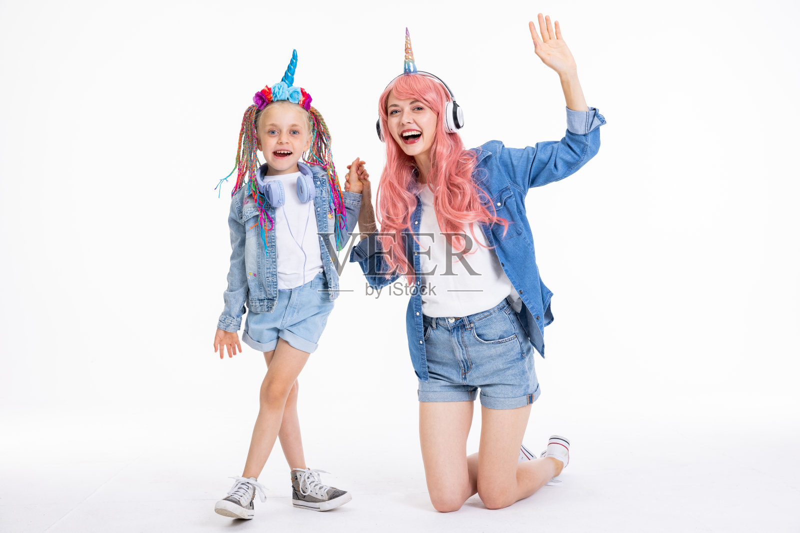 美丽的年轻母亲，戴着粉红色的假发和独角兽发带，双手抱着漂亮的学龄前女儿，扎着五颜六色的辫子。女孩们在摄影棚里摆姿势拍照照片摄影图片