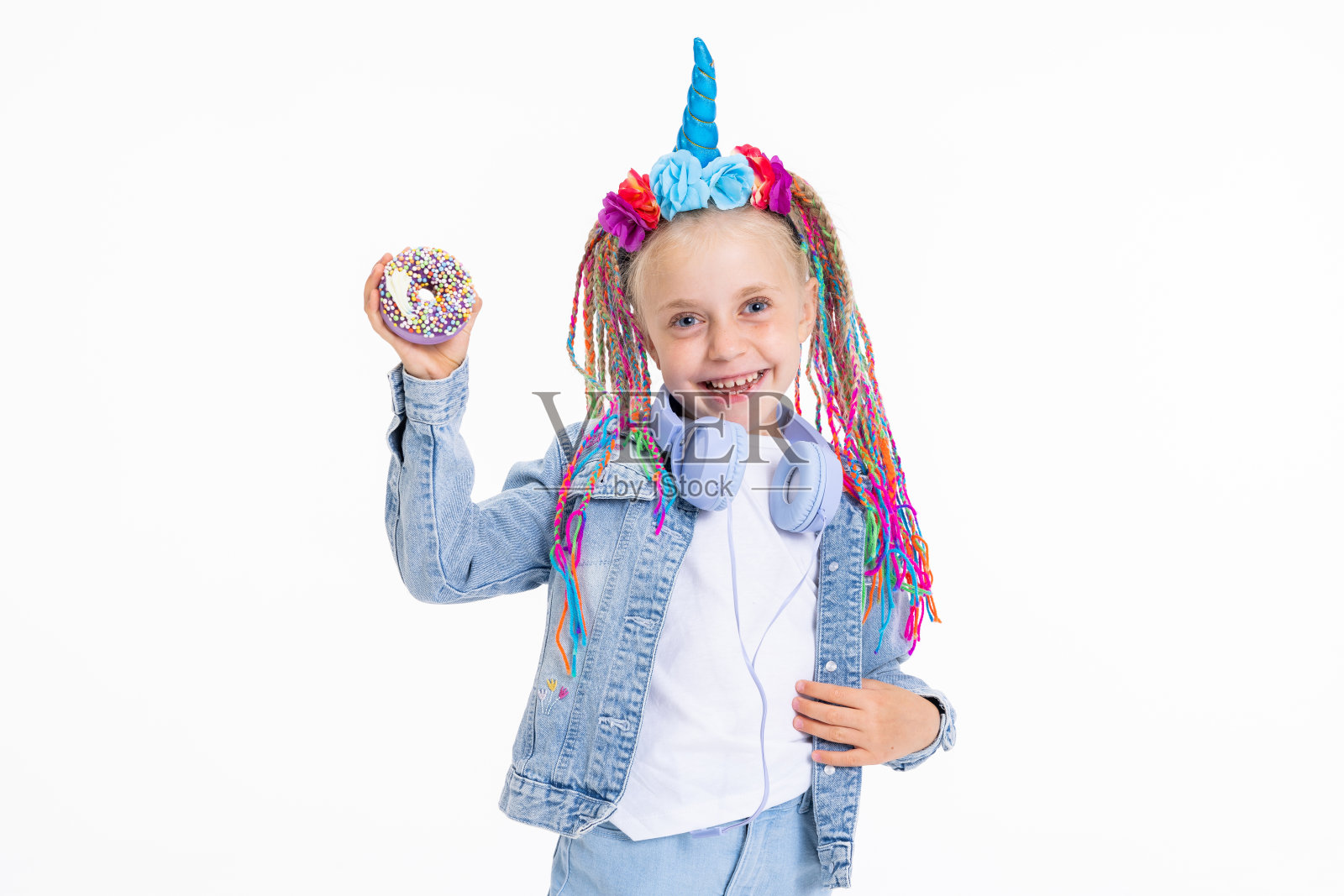 漂亮的小女儿穿着牛仔衣服和白色纯色t恤，扎着彩色的辫子，戴着独角兽发带，手里拿着巧克力甜甜圈，在拍摄过程中在镜头前摆姿势照片摄影图片