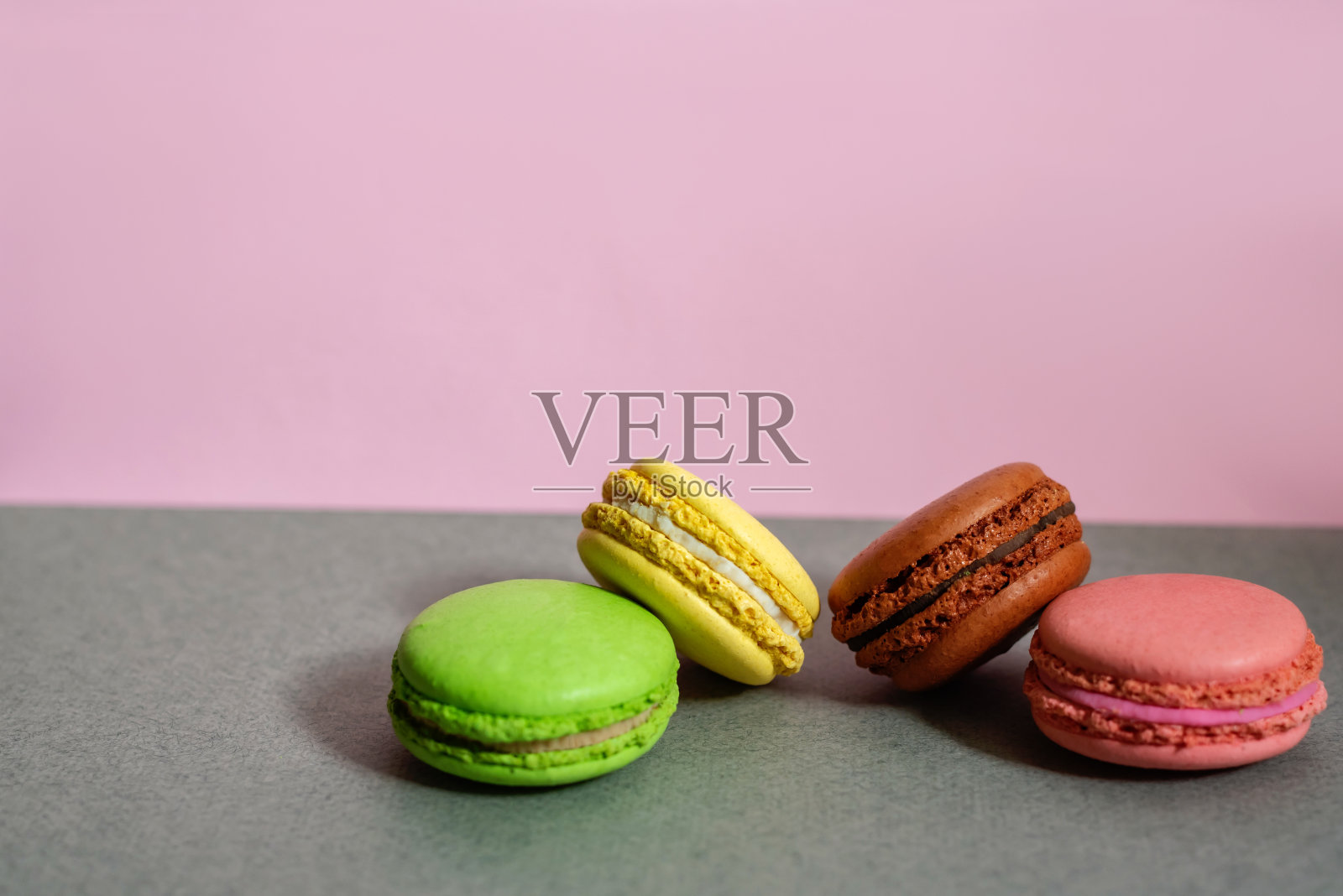 一组不同颜色的马卡龙躺在粉灰色的背景。放文字的地方。照片摄影图片