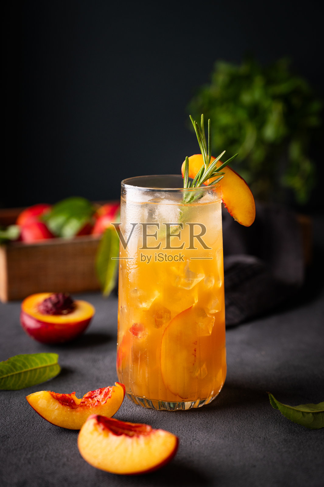 桃子茶加冰和迷迭香，高脚杯。纯素自制健康饮料，暗底配新鲜水果。照片摄影图片