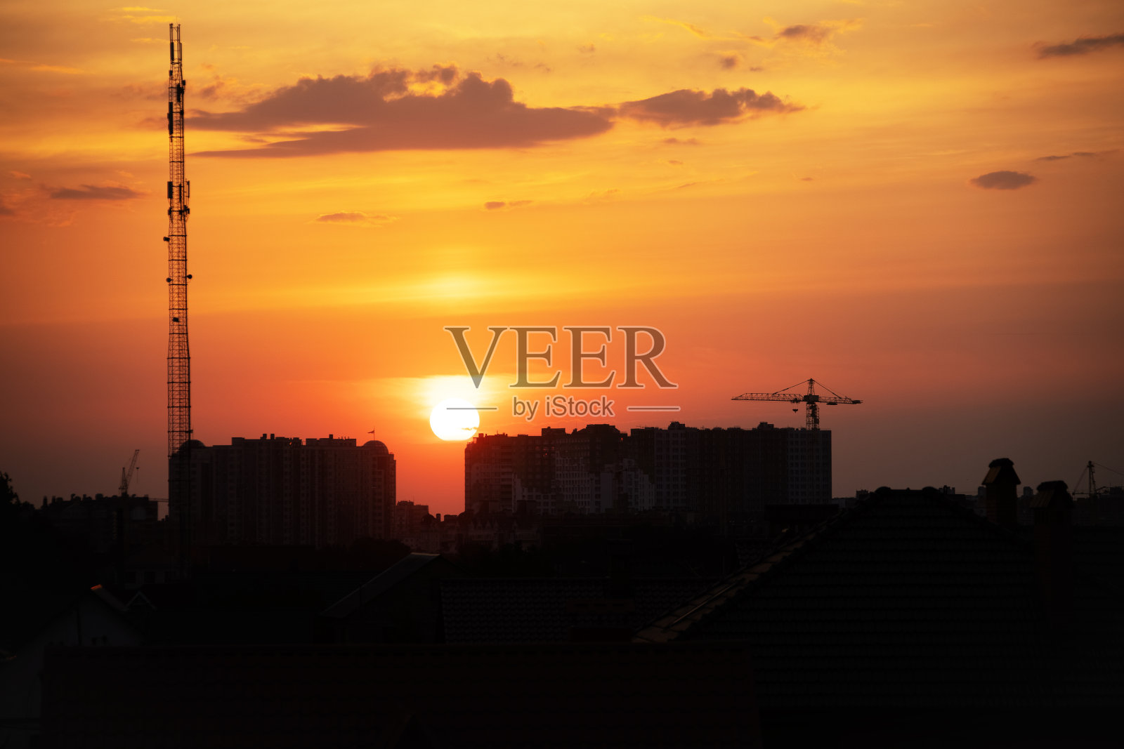 在落日的余晖中，有烟囱和管道的房屋屋顶的黑暗、清晰的剪影。日落在城市。夕阳背光下的城市景观剪影。景观的天空。照片摄影图片