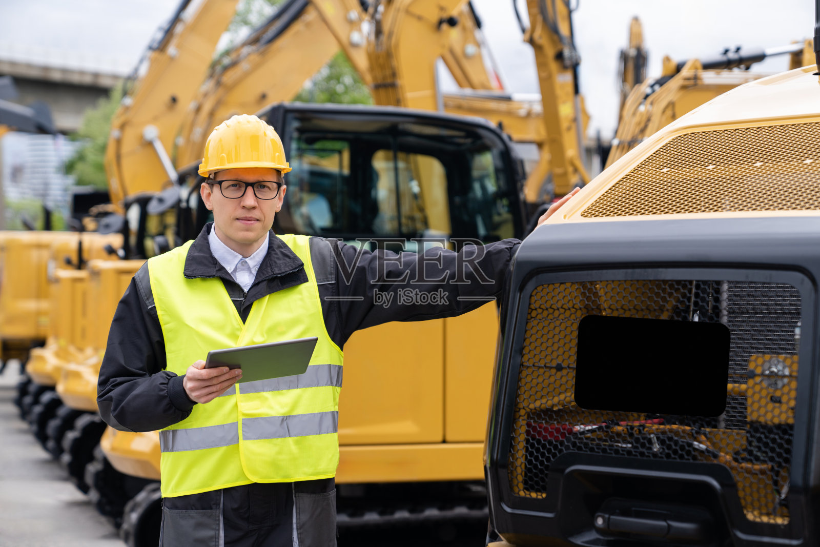 一位拿着平板电脑的工程师站在建筑挖掘机旁边照片摄影图片