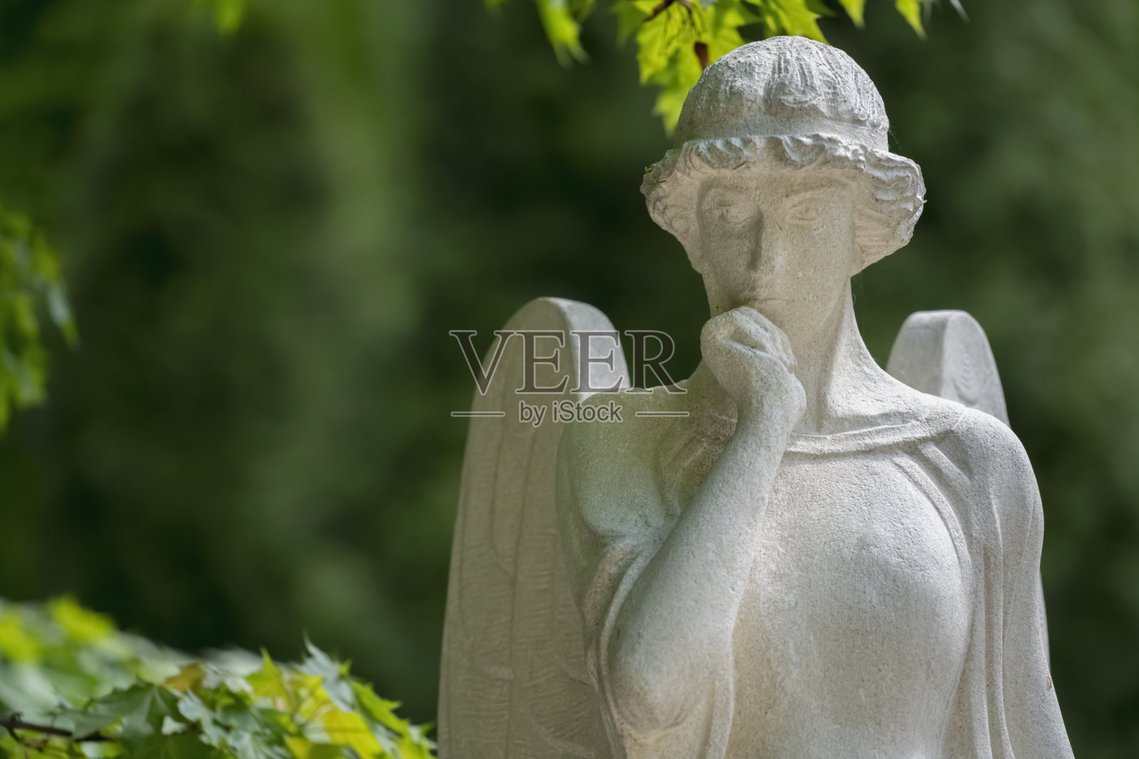 美丽的白色天使在绿色的树叶背景下。古代石像的碎片。照片摄影图片
