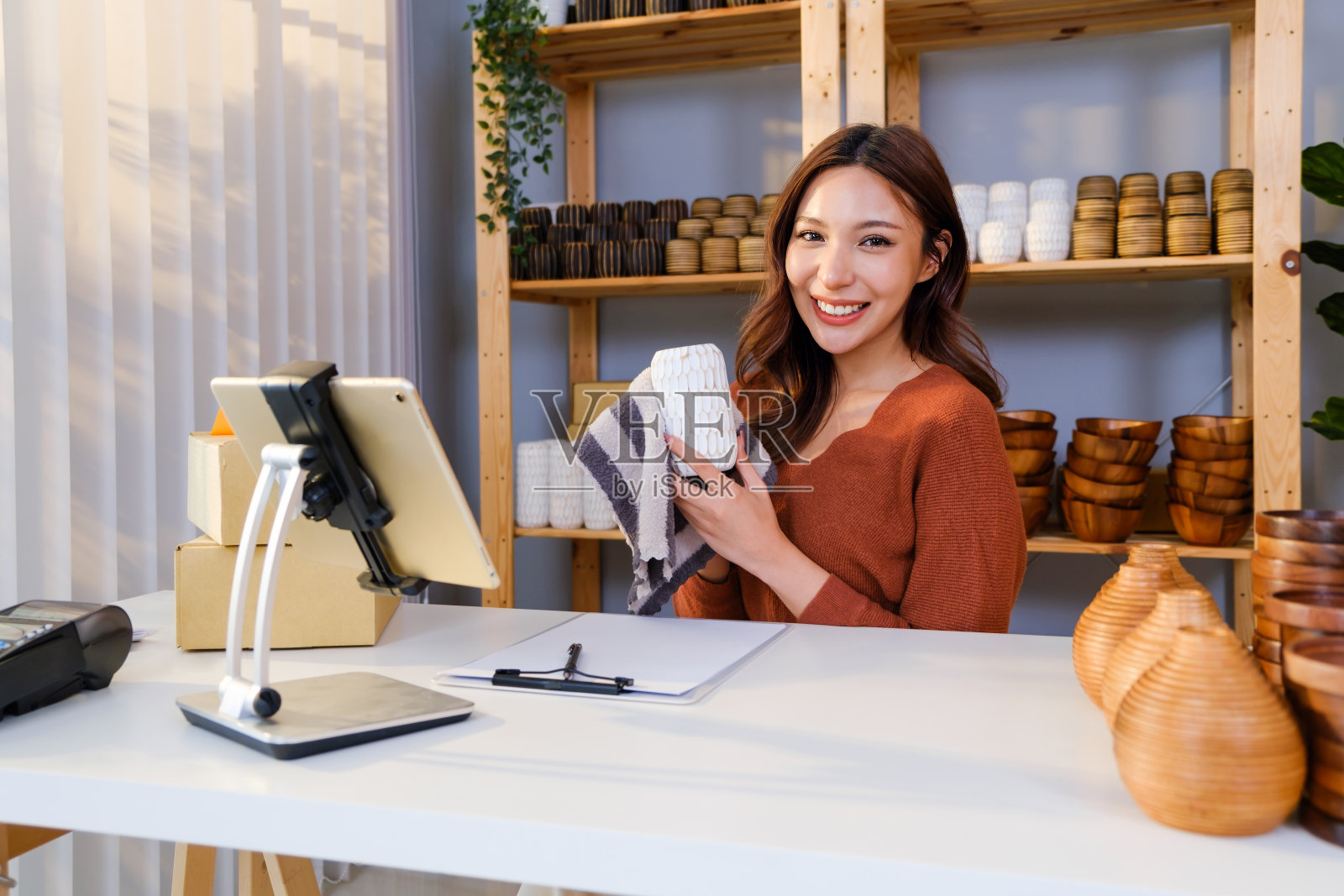 亚洲美女在家搓卖花瓶产品在线直播。年轻迷人的女孩用智能手机向顾客详细展示商品。远程购买和网上购物的概念。照片摄影图片