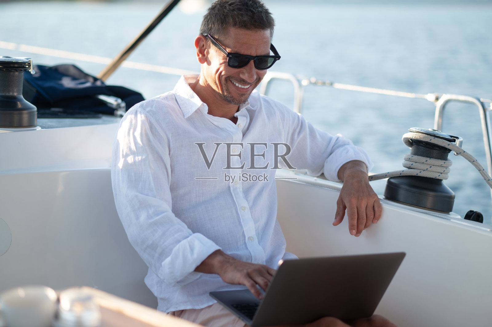 戴着墨镜的微笑男子在游艇上上网照片摄影图片