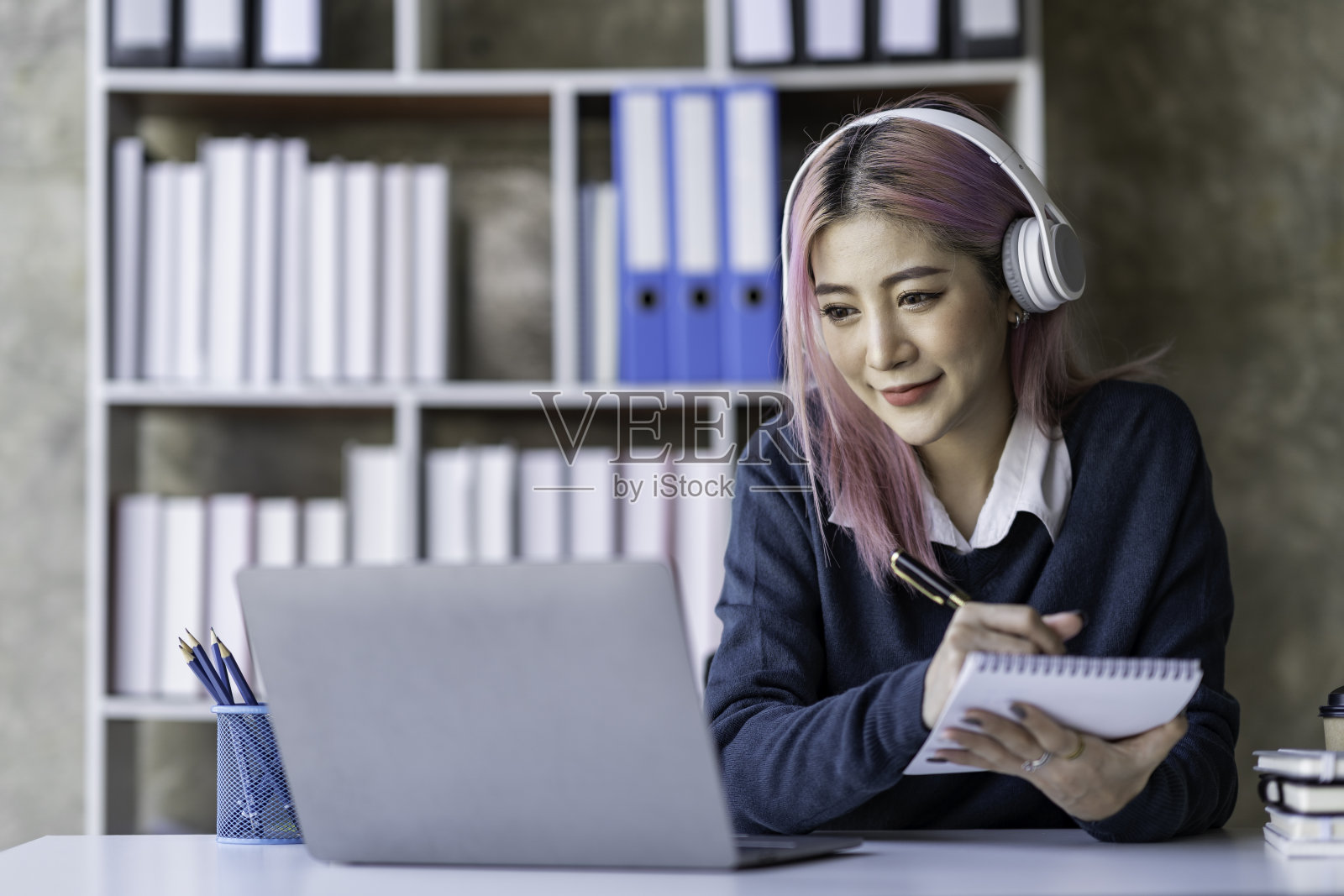 美丽的亚洲女商人戴着耳机在笔记本电脑和智能手机上进行视频通话，记录产品信息、收入和在线商业理念。照片摄影图片