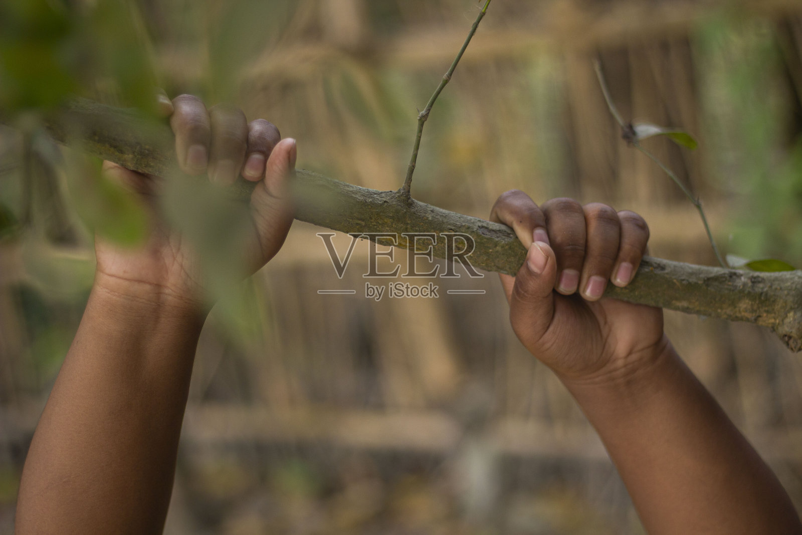 一个男孩用双手握着一根粗树枝，背景模糊照片摄影图片