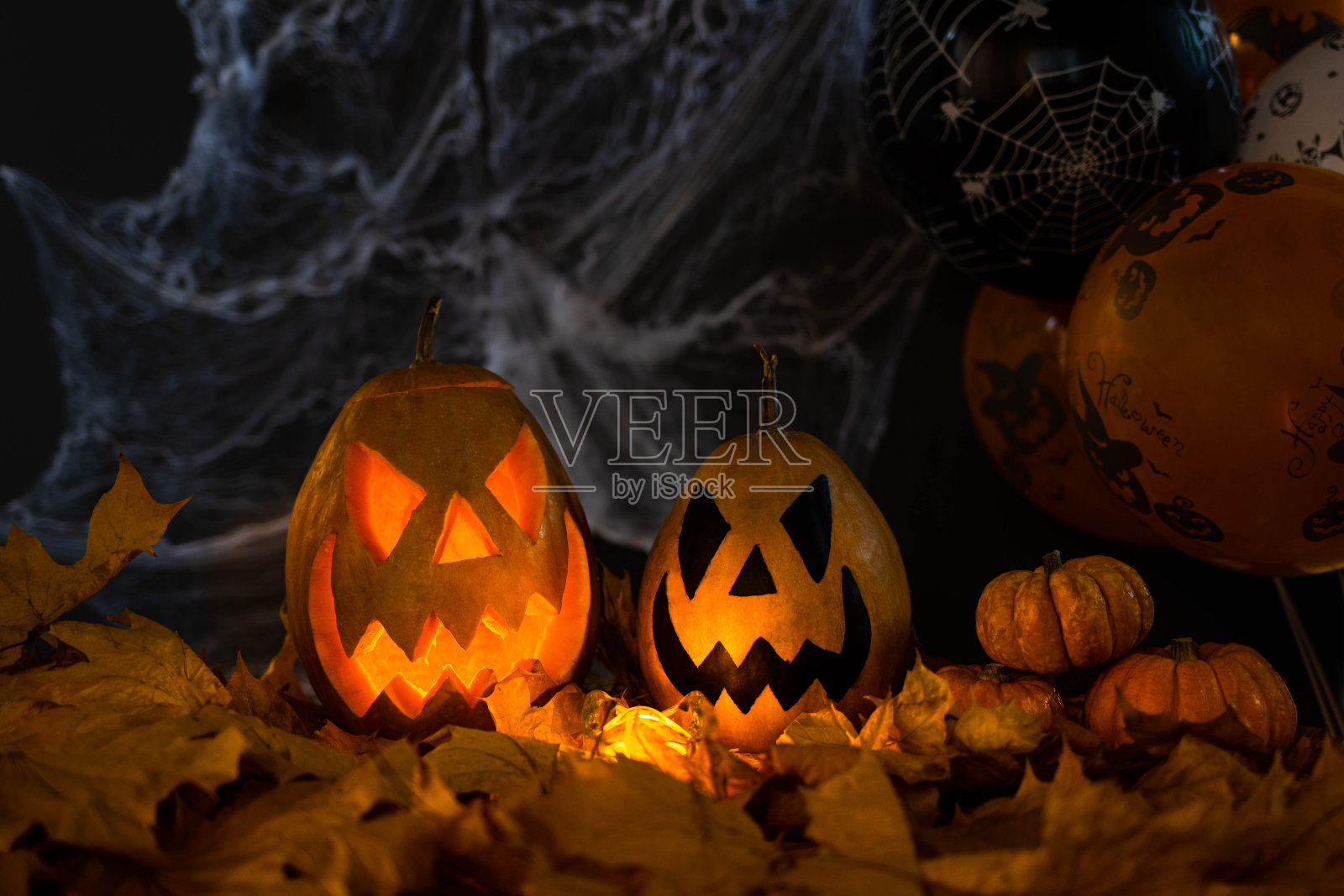 万圣节的节日属性。由南瓜雕刻而成的南瓜灯在黑暗中发光，黑色的背景上有蜘蛛网、秋叶和气球。不给糖就捣蛋照片摄影图片