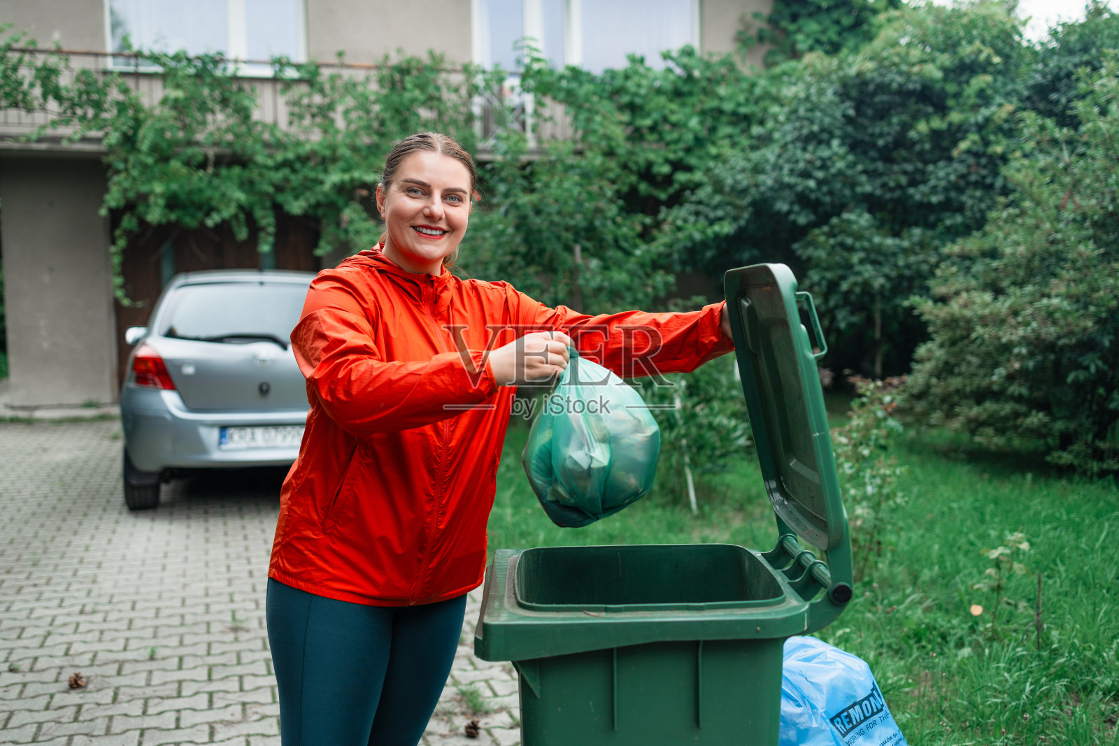 一名白人妇女正在整理垃圾，把一个装有垃圾的袋子扔进一个小型的户外回收站照片摄影图片