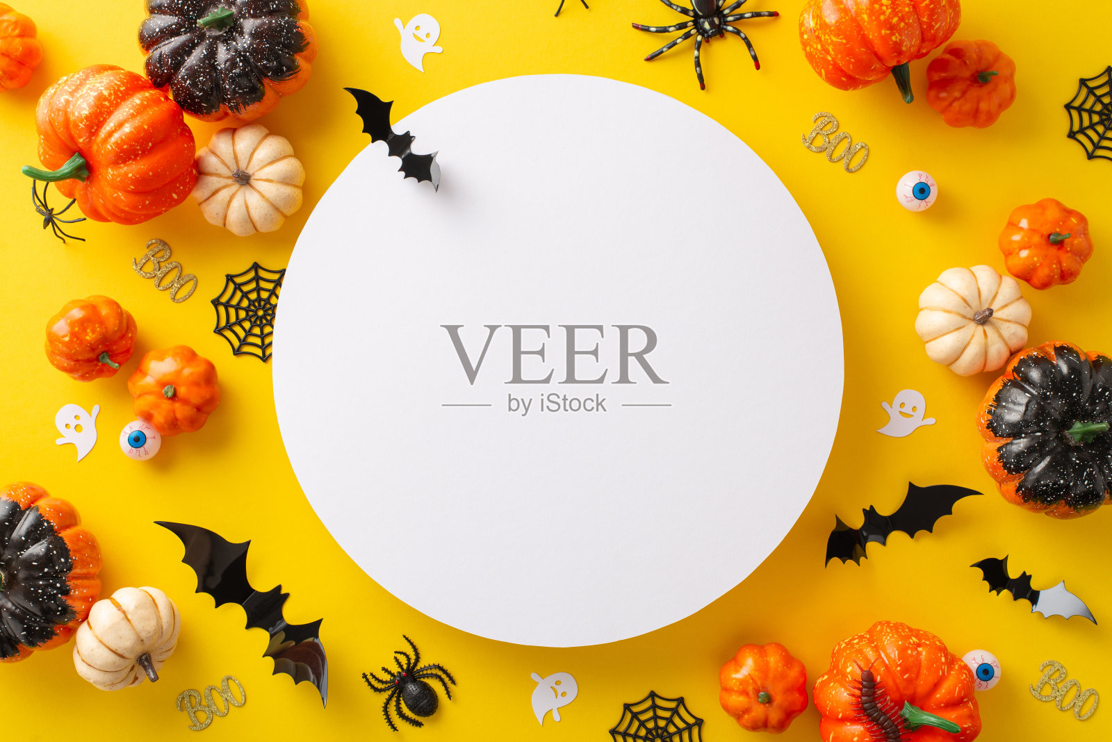 沉浸在诡异的万圣节夜晚。高角度拍摄展示南瓜，纸鬼和蝙蝠和万圣节装饰在一个黄色孤立的表面。非常适合广告或文本照片摄影图片