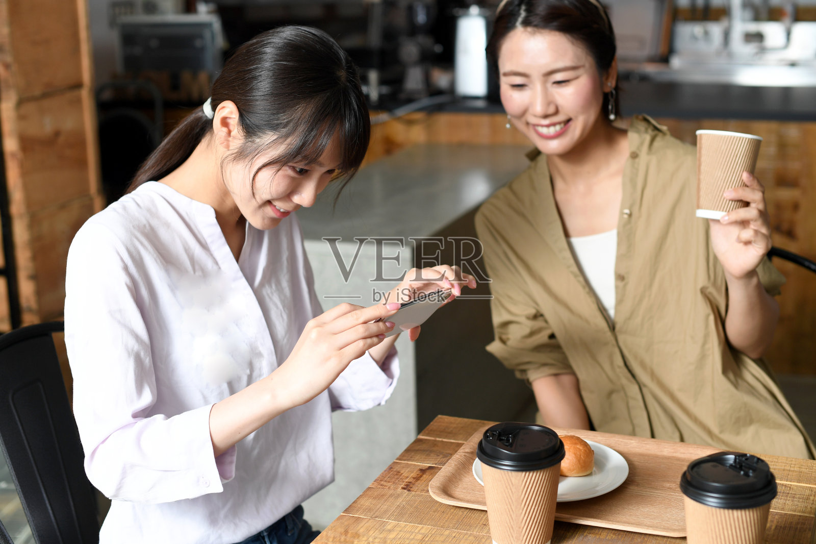 微笑的年轻亚洲女性在咖啡馆用智能手机拍摄食物照片摄影图片