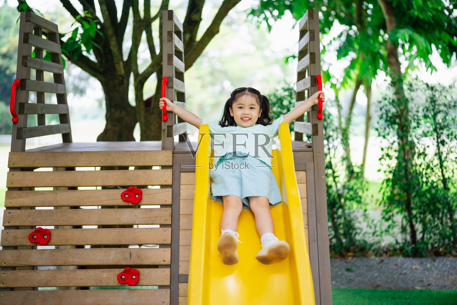可爱的亚洲女孩微笑玩耍在学校或幼儿园的院子或操场。儿童健康的夏季活动。亚洲小女孩在户外操场上攀爬。孩子在户外操场上玩耍。照片摄影图片