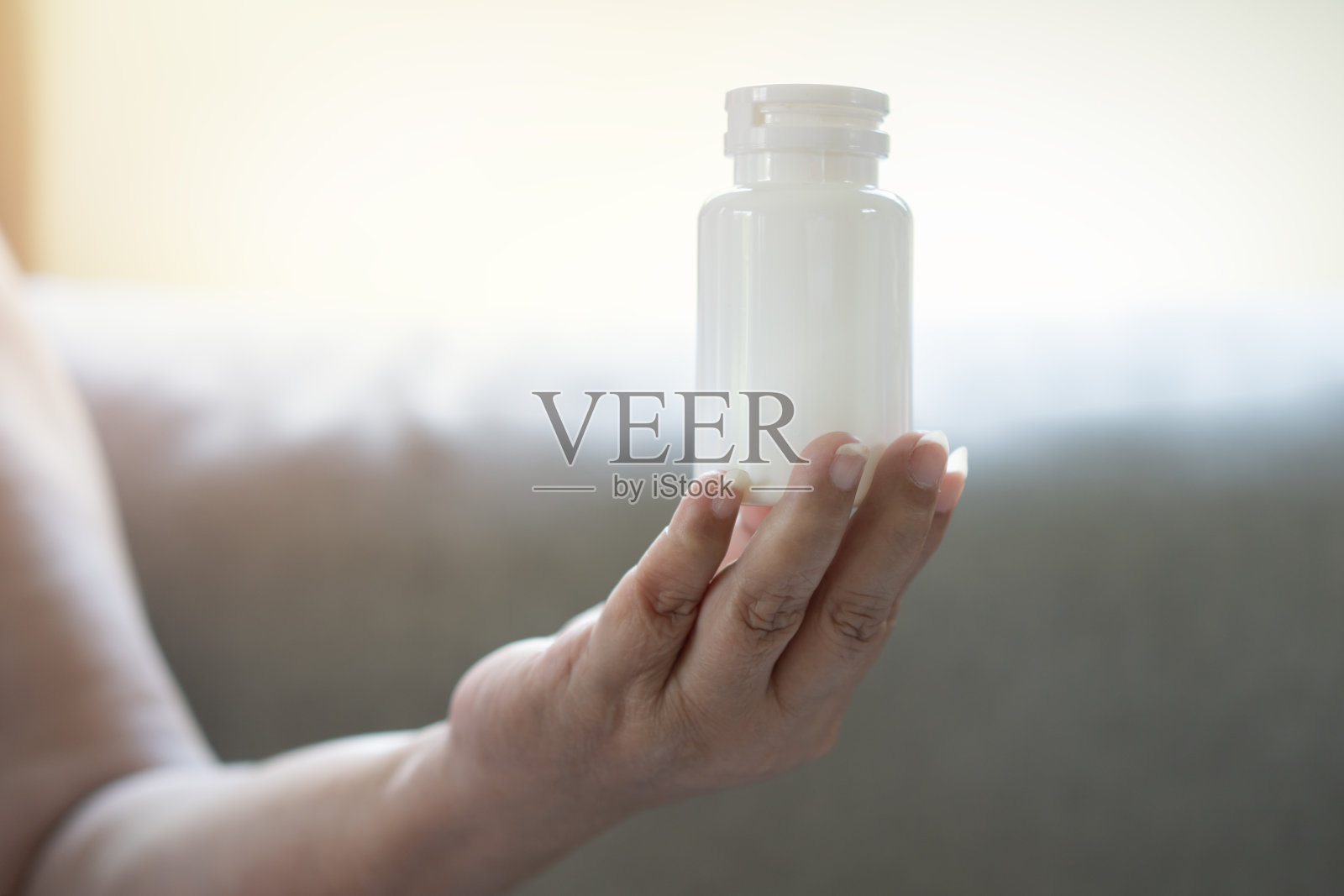 年长的女性坐在家里的沙发上，手里拿着空白的白色挤压瓶塑料管。照片摄影图片