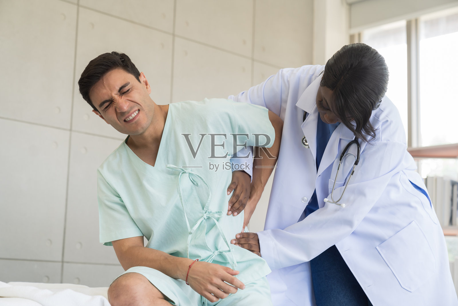 女护士在医院病床上照顾小心翼翼的男病人。女助理在诊所照顾背部疼痛的男病人照片摄影图片