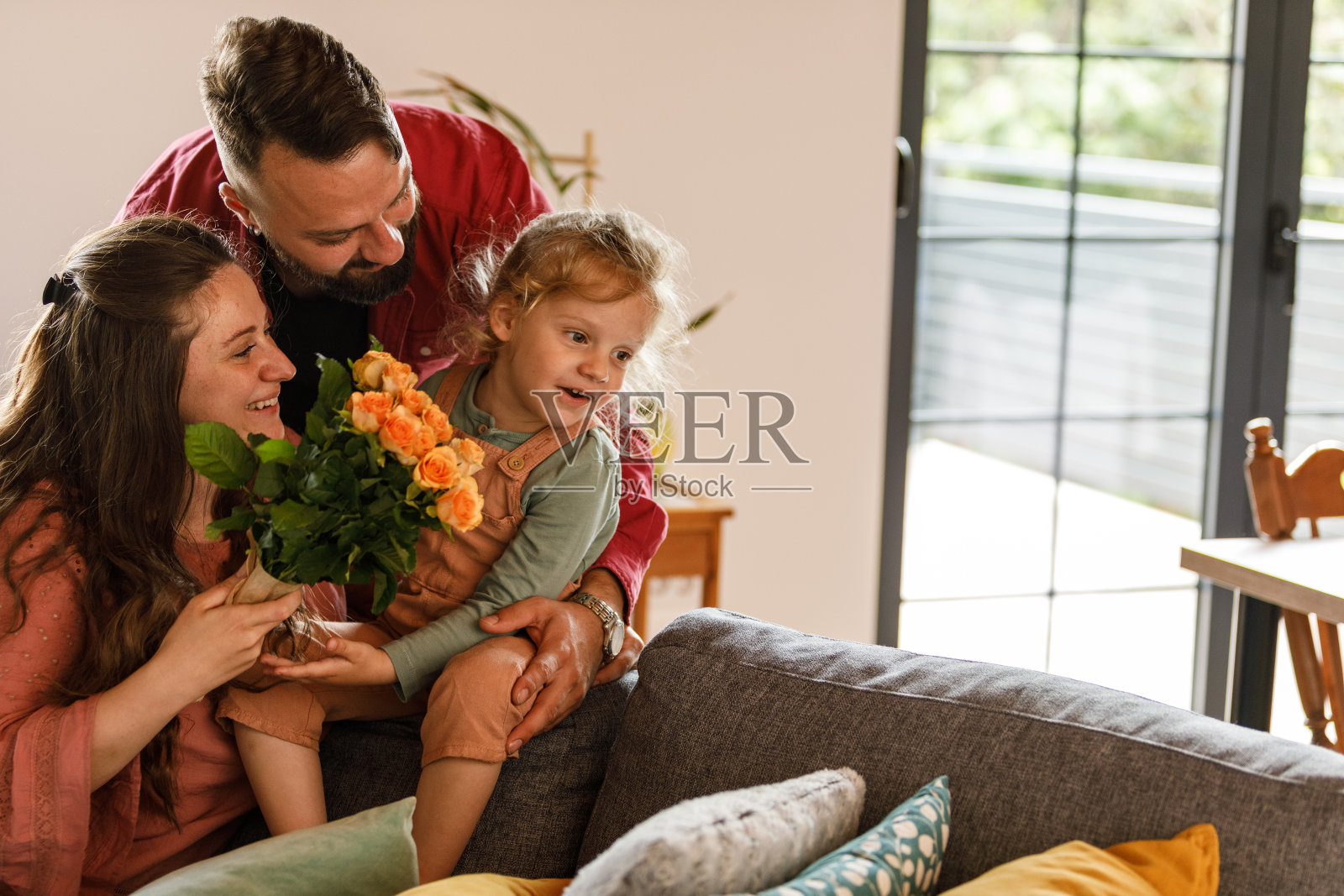 母亲在收到母亲节的鲜花后，抱着蹒跚学步的孩子和丈夫照片摄影图片