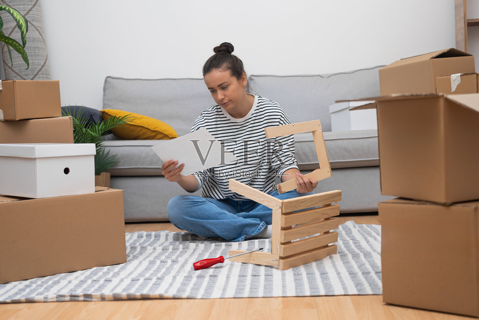 新房子地板上的女人，在移动的纸箱和家具中自组装货架照片摄影图片