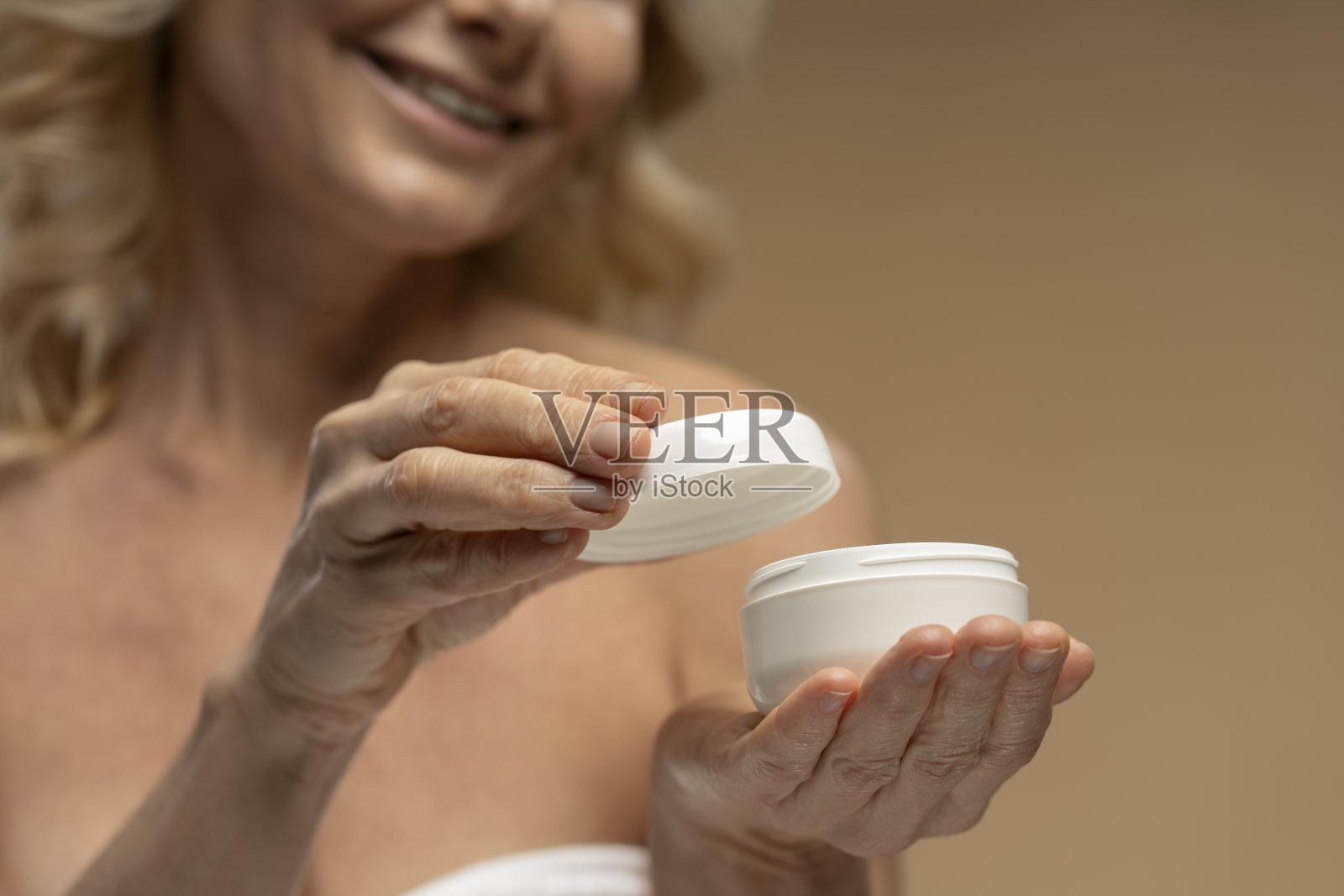 专注于双手模糊的成熟女性打开一罐保湿化妆品，米色背景照片摄影图片