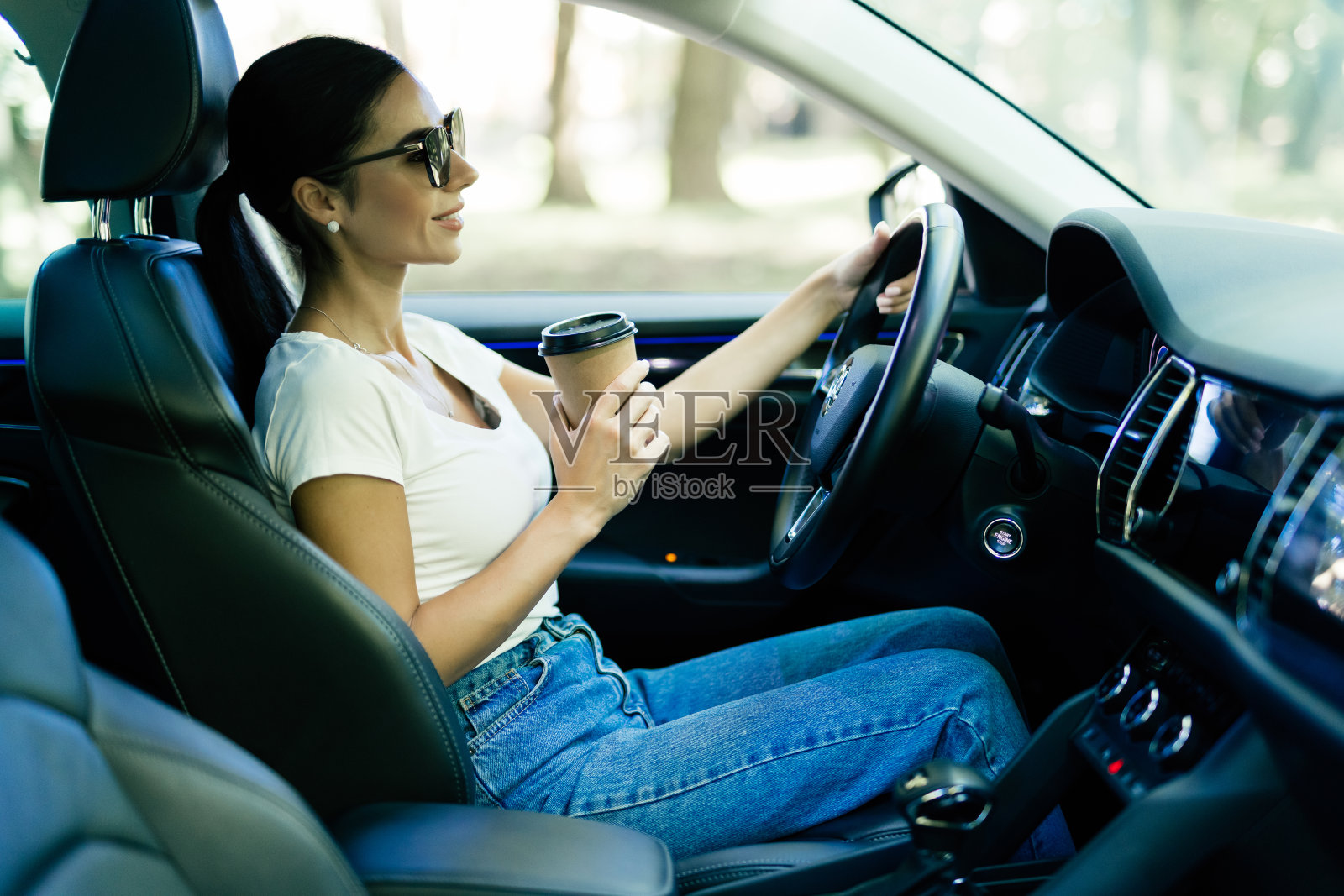 快乐的年轻女人带着咖啡去开车。一边开车一边喝咖啡的女人。照片摄影图片