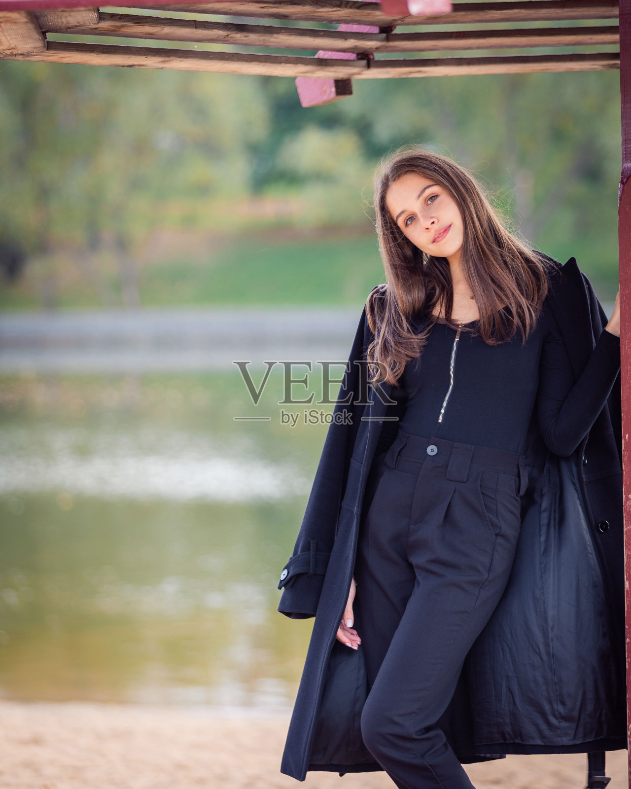 一个美丽的女孩在秋天的公园里撑着伞站在池塘边。照片摄影图片