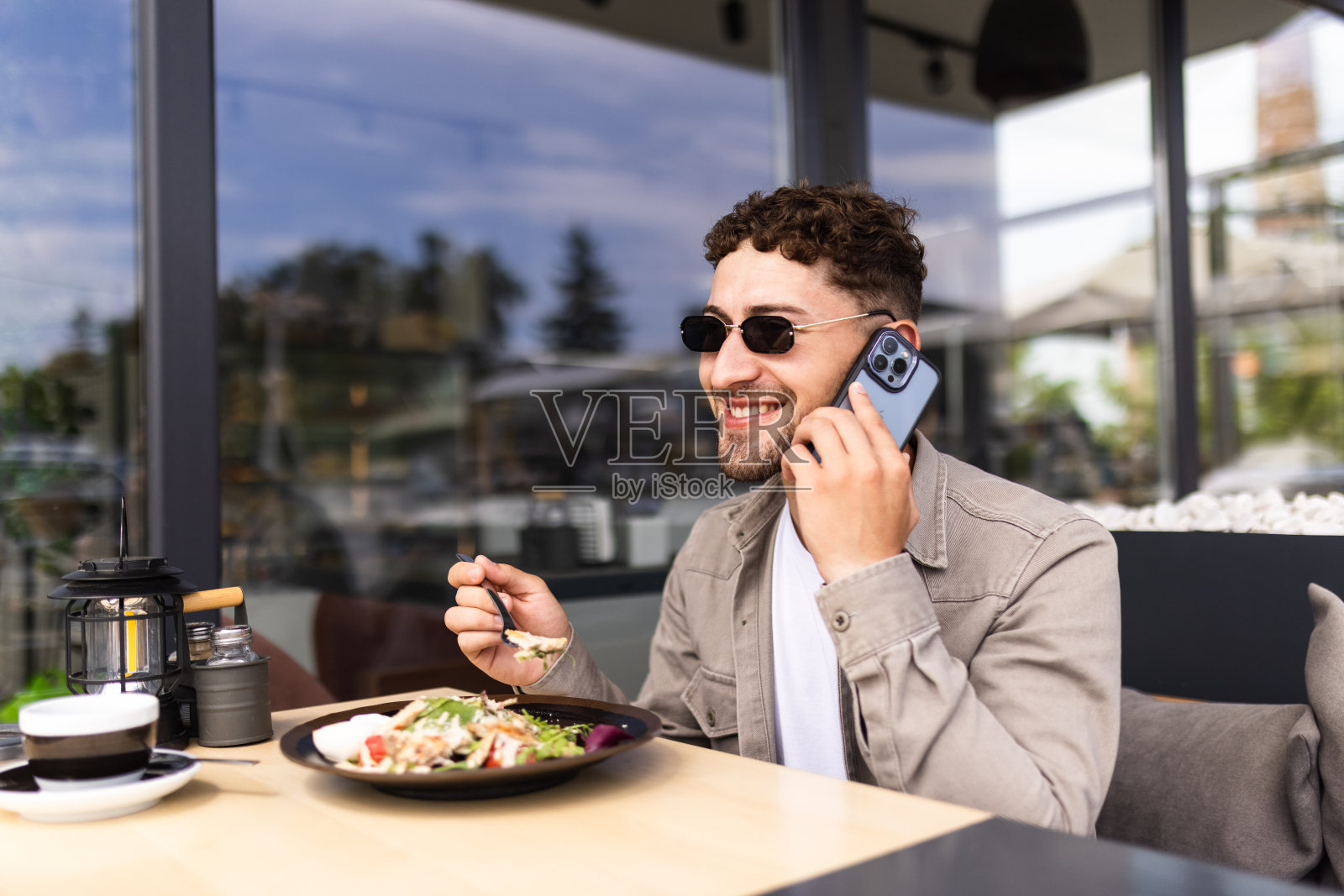帅哥一边在餐厅吃着美味的沙拉一边讲着手机，面带微笑照片摄影图片