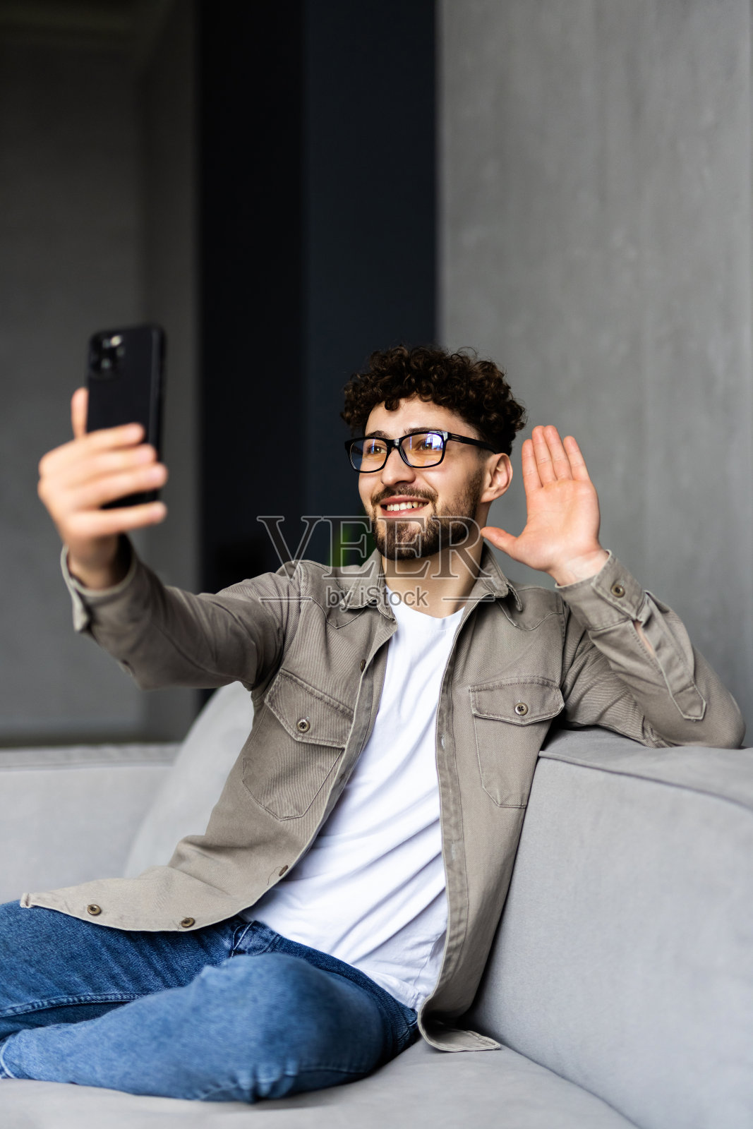 在线视频通话。积极的人对着摄像头挥手，与朋友或家人愉快地交谈。男人微笑着，享受着远方的交流，坐在地板上，倚在沙发上照片摄影图片