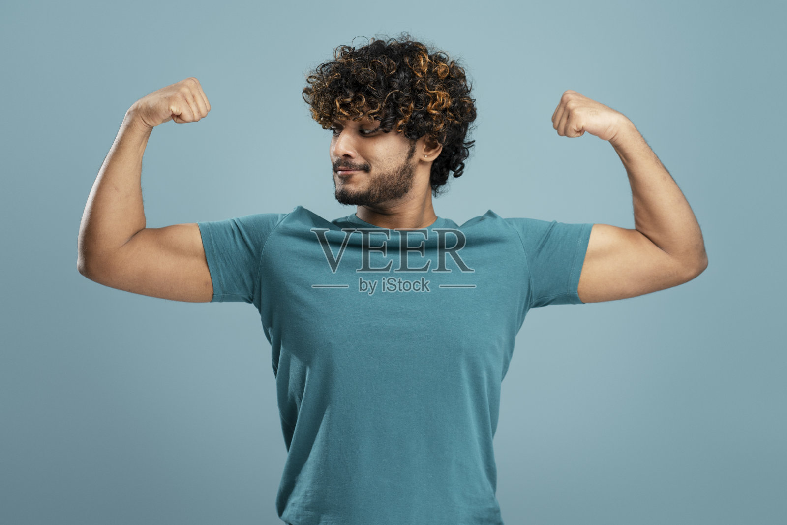 年轻的印度健身男子穿着休闲的蓝色t恤，在孤立的背景下展示手臂肌肉。照片摄影图片