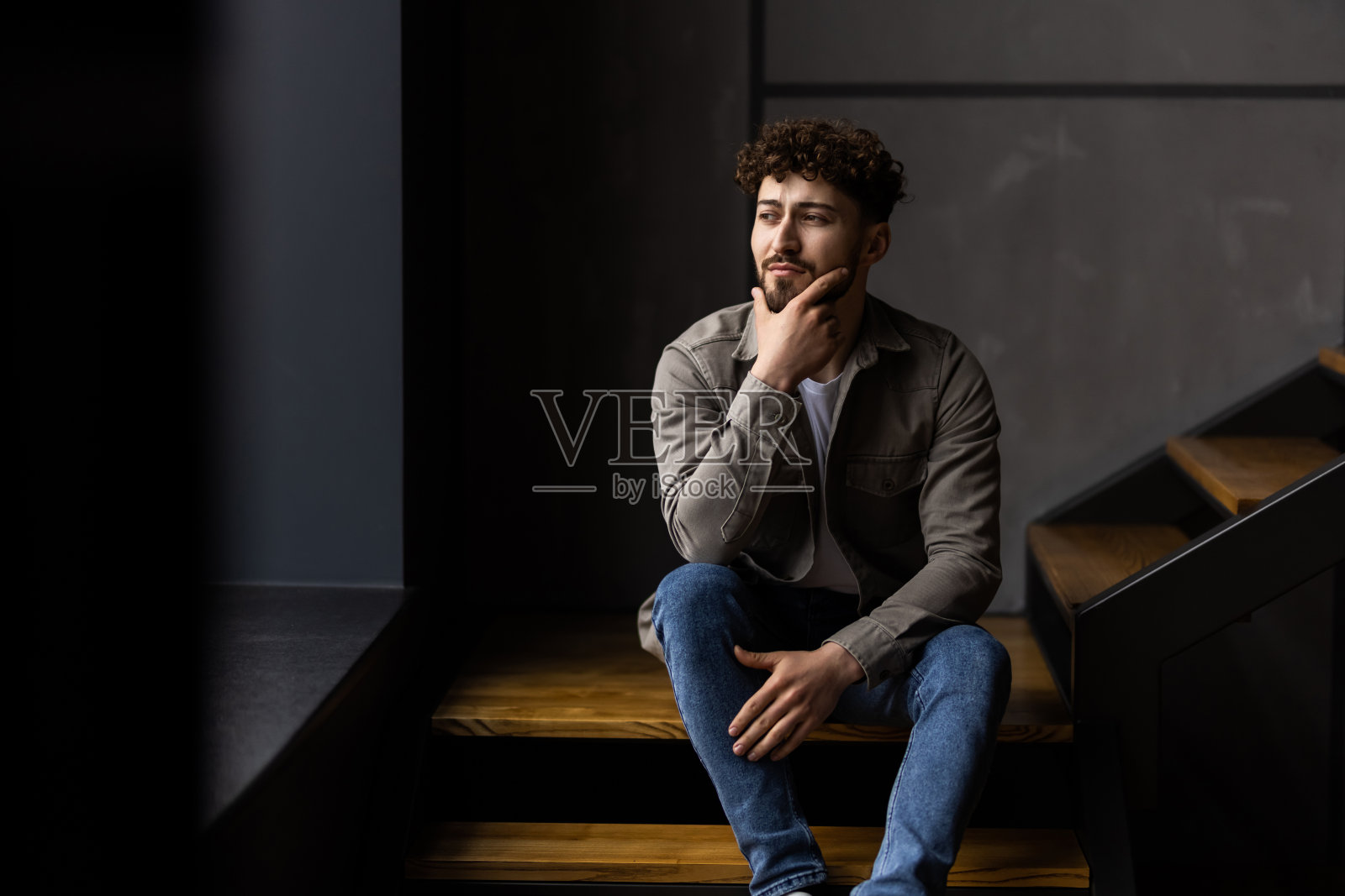 一个年轻人坐在家里的楼梯上。照片摄影图片