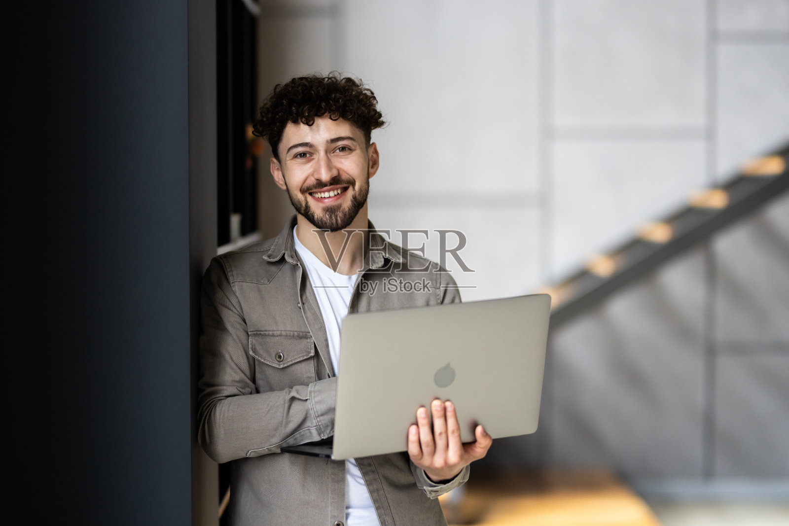 帅哥办公室职员的肖像，手里拿着笔记本电脑站在办公室里照片摄影图片