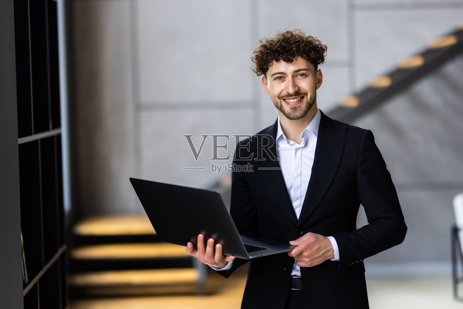 年轻的商人站在办公室，手里拿着打开的笔记本电脑，微笑着浏览网站照片摄影图片