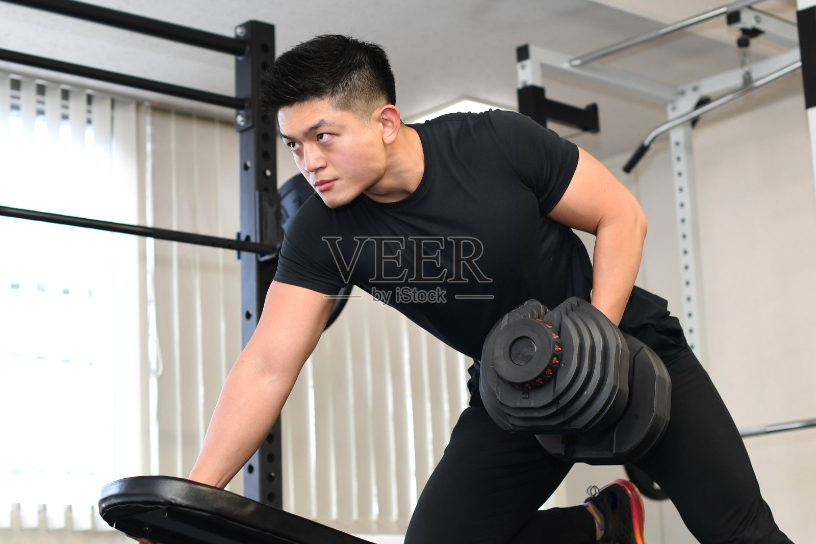 年轻的亚洲男子在健身房拿着哑铃做划船训练照片摄影图片