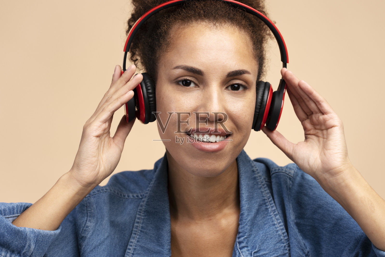 近距离特写，微笑着的多民族妇女戴着无线耳机，看着相机，米色背景照片摄影图片