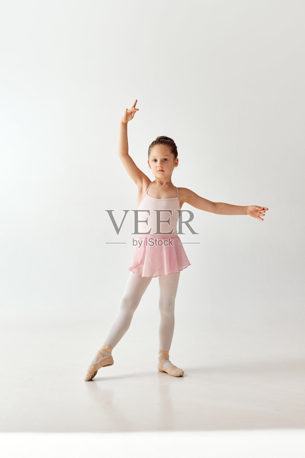 小漂亮的学龄前芭蕾舞女舞者的肖像，穿着玫瑰色的芭蕾舞裙，白色的绑腿，站在白色的背景上，手牵着手。照片摄影图片