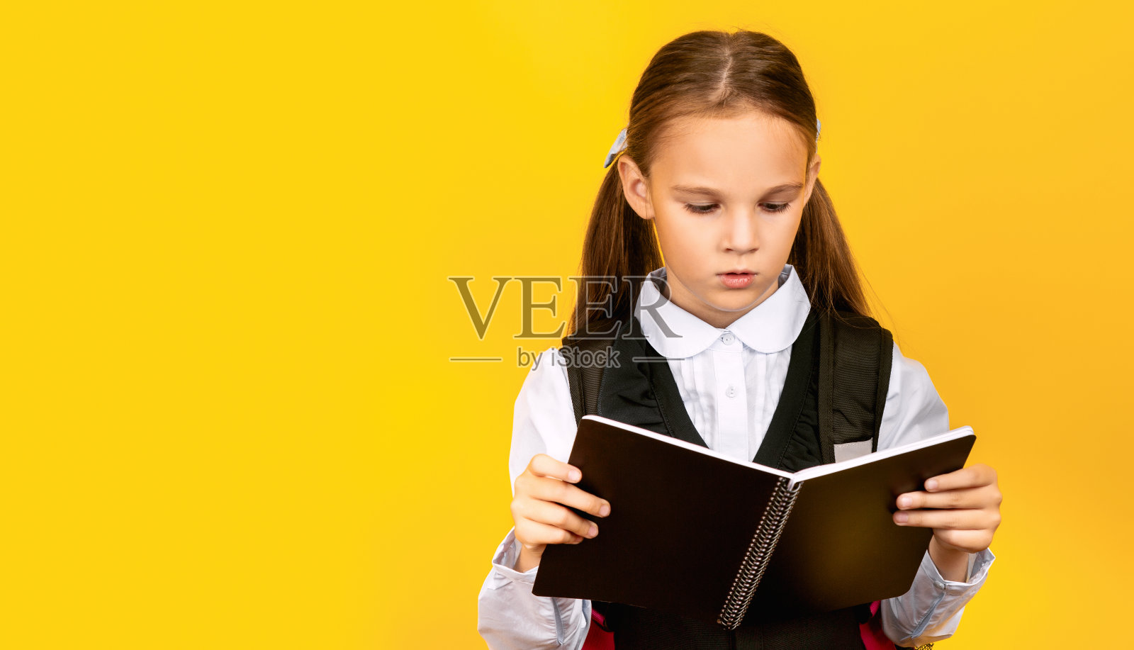 一个女学生站在黄色背景的摄影棚里，手里拿着为《返校》准备的书。学校教育理念照片摄影图片