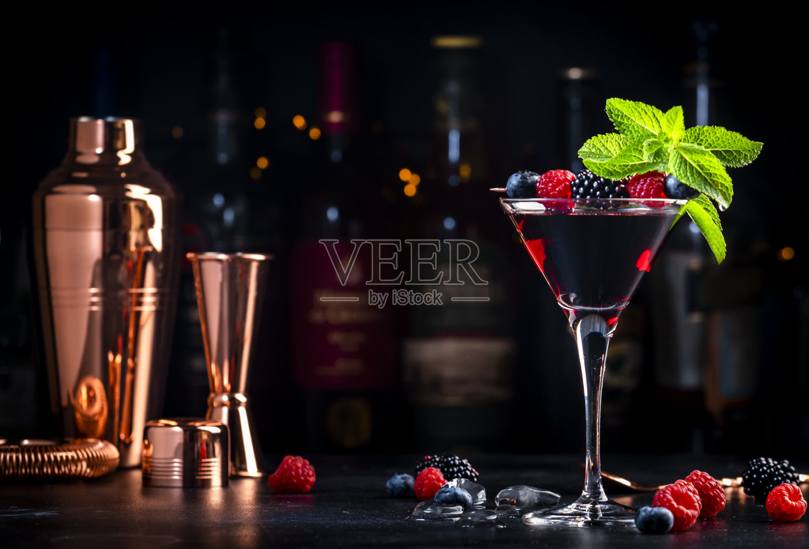 野生浆果-黑色鸡尾酒饮料与伏特加，糖浆，柠檬汁，蓝莓，覆盆子，黑莓和冰在鸡尾酒杯，深色吧台背景，工具和瓶子照片摄影图片