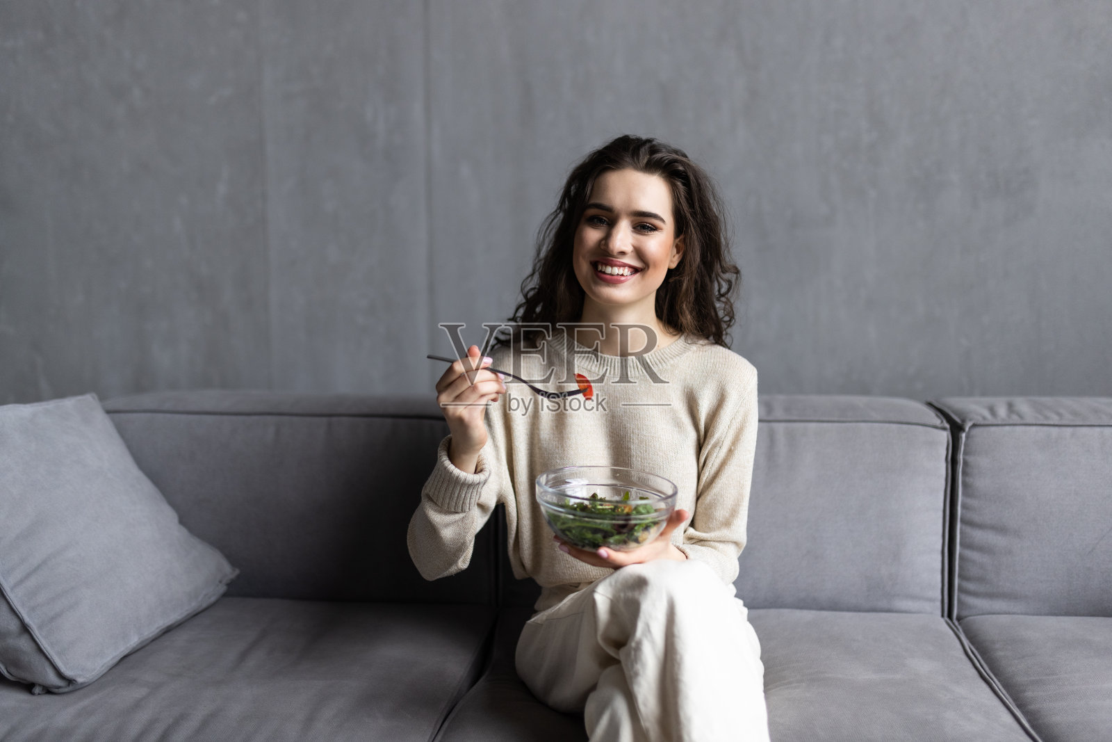 快乐的年轻女子躺在沙发上，在客厅里吃着沙拉照片摄影图片