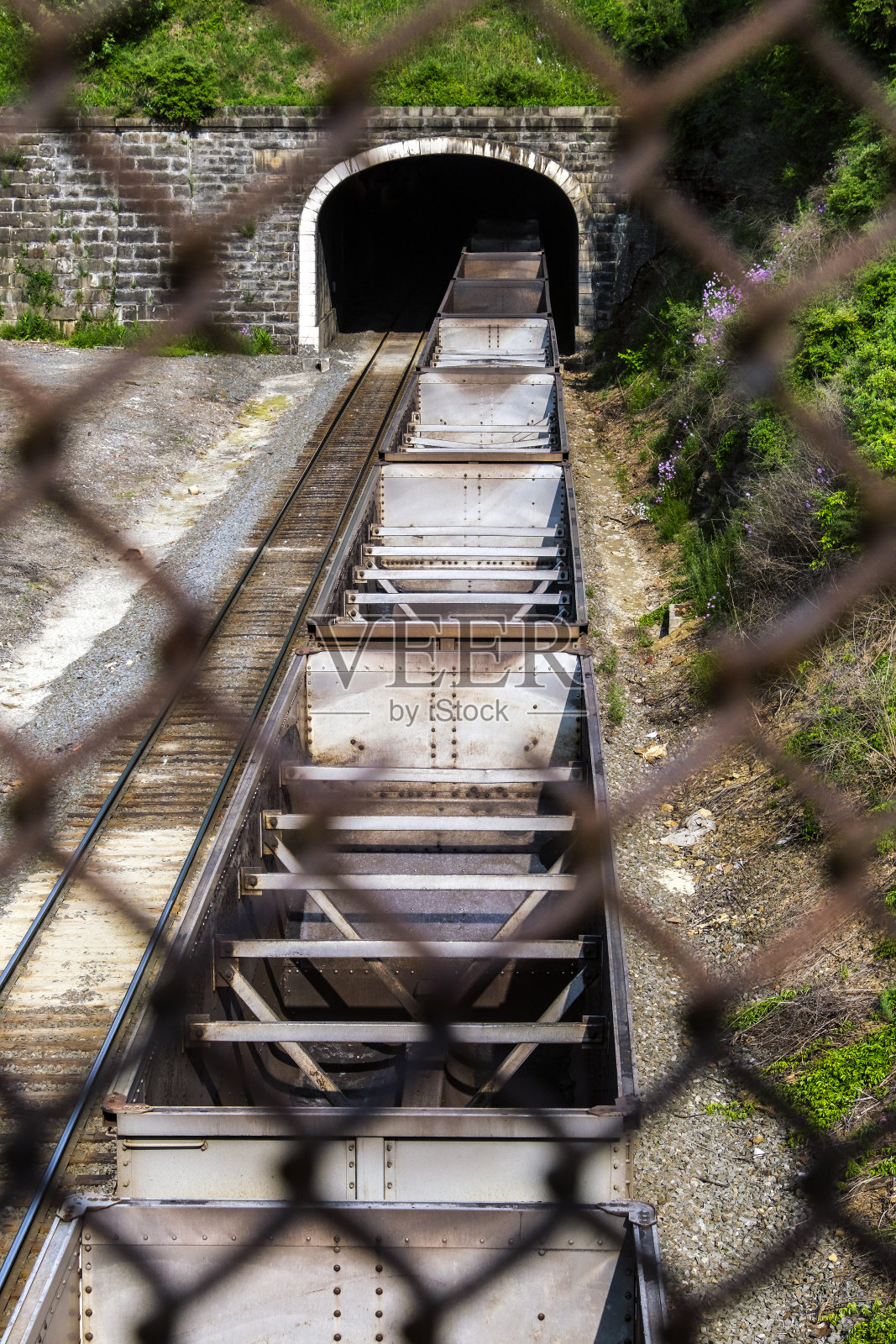 空煤列车通过石砌拱门的双线铁路隧道时，铁丝网安全围栏缝隙内的景象照片摄影图片