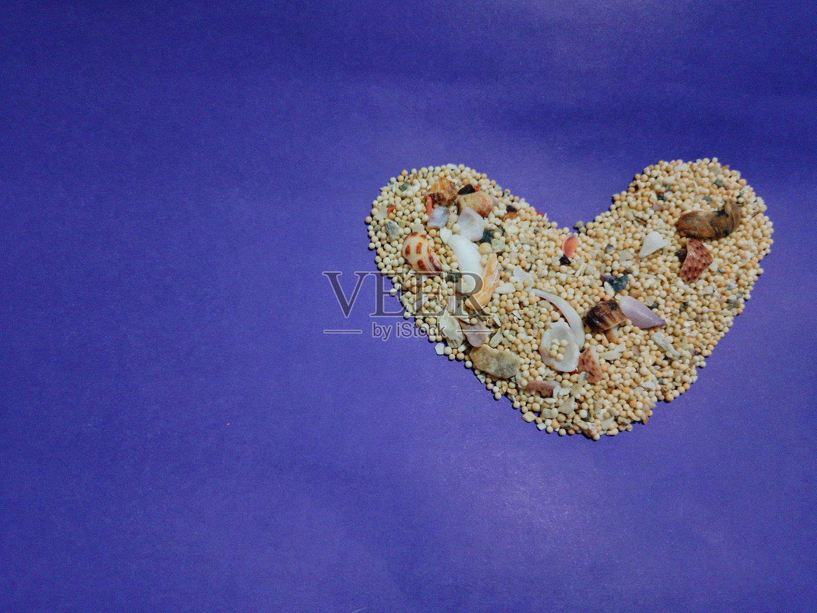 龙目岛塞梅蒂海滩的沙子堆成心形，紫色背景照片摄影图片