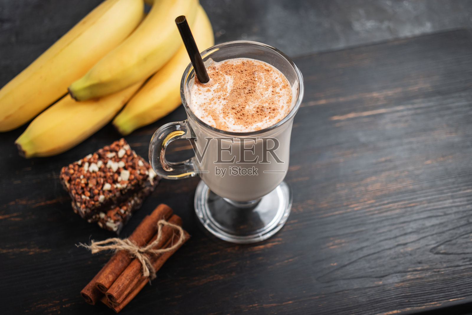一杯带吸管的蛋白奶昔和一勺乳清蛋白粉，深色木板上的蛋白棒和香蕉，健身食品补充剂照片摄影图片