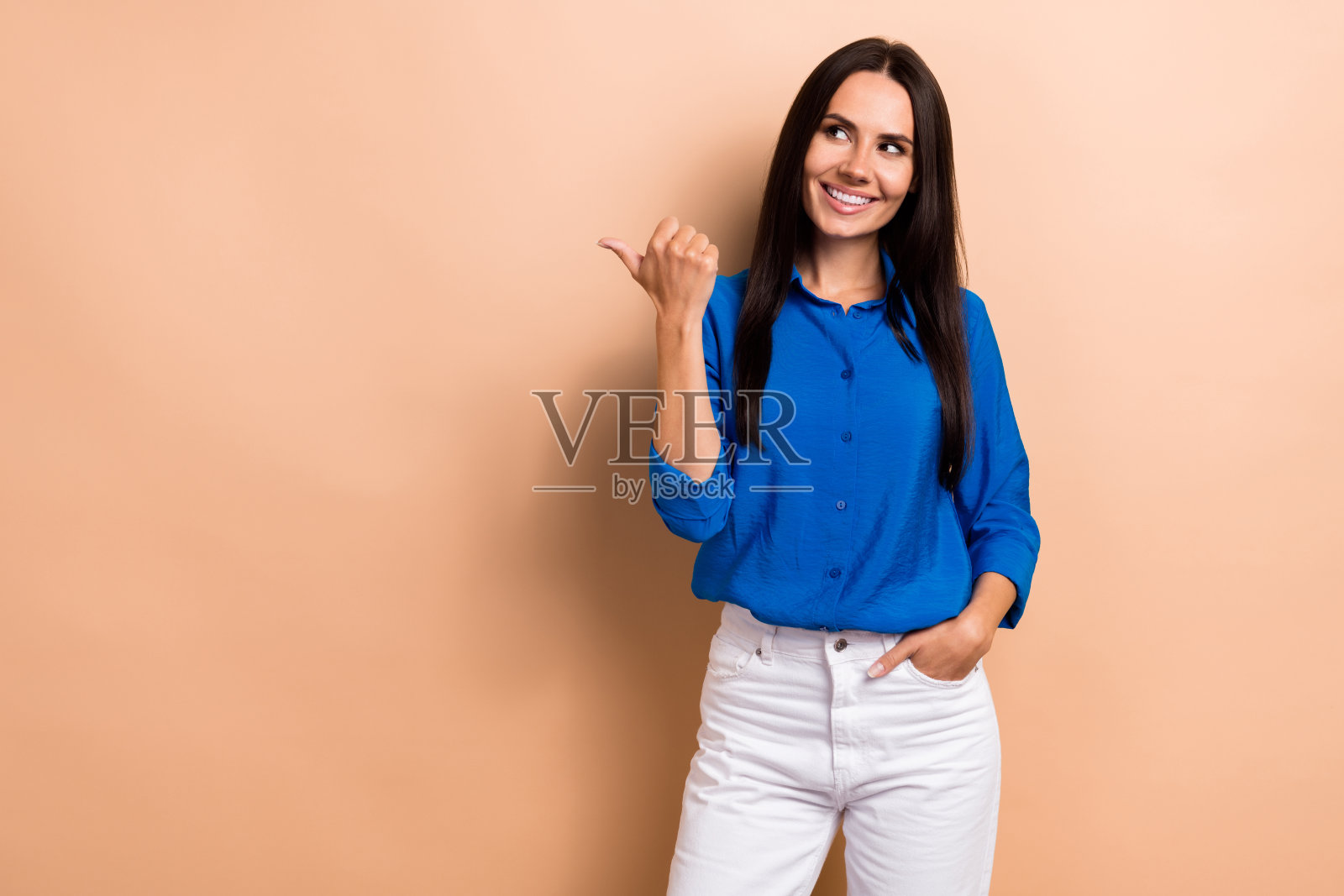 照片中开朗可爱的女孩穿着时尚的衣服，手臂指向空旷的空间，呈现出米色背景上孤立的海报照片摄影图片